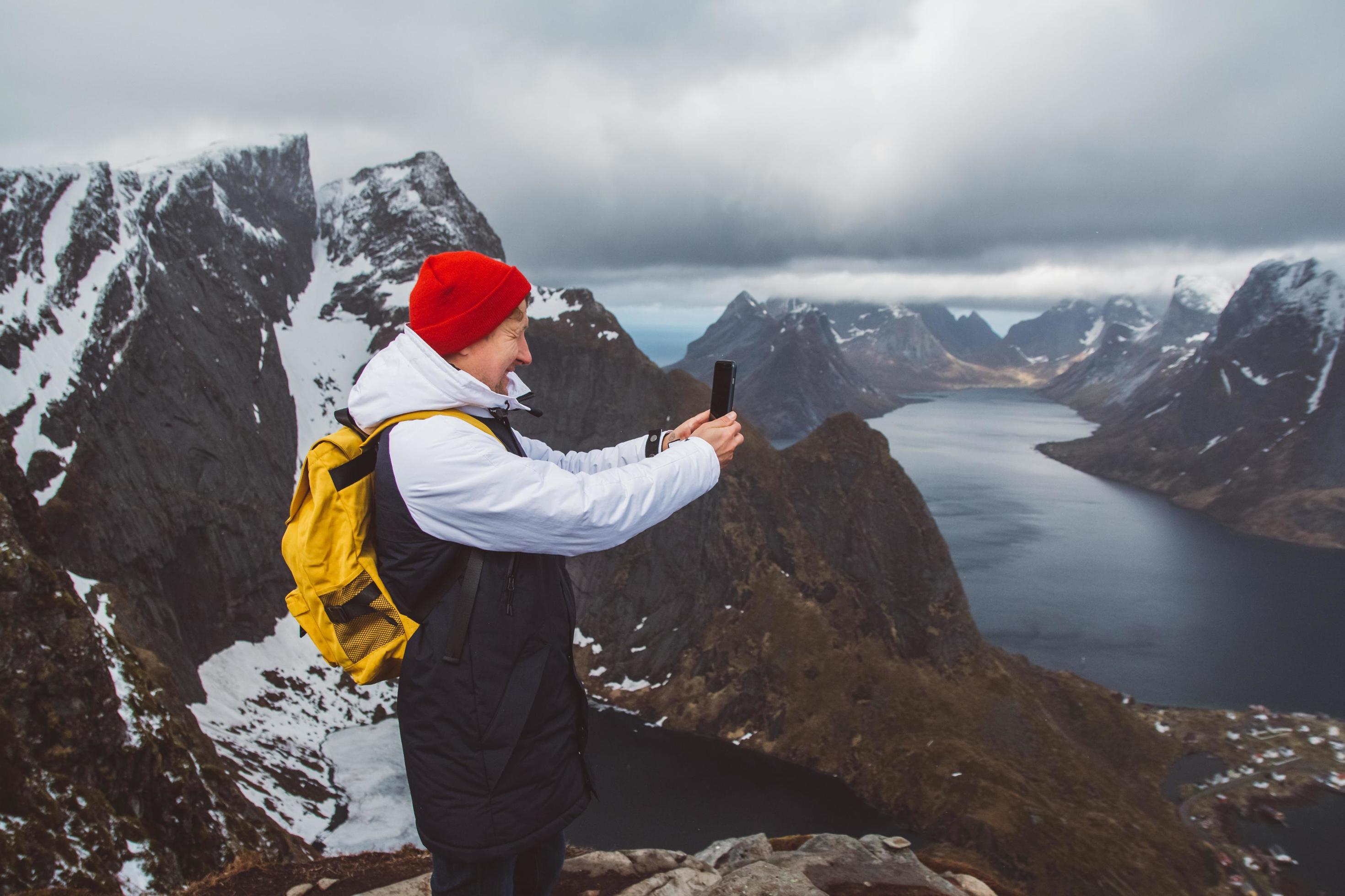 Man traveler taking photo with a smartphone hiking on Reinebringen mountain ridge in Norway lifestyle adventure traveling Stock Free