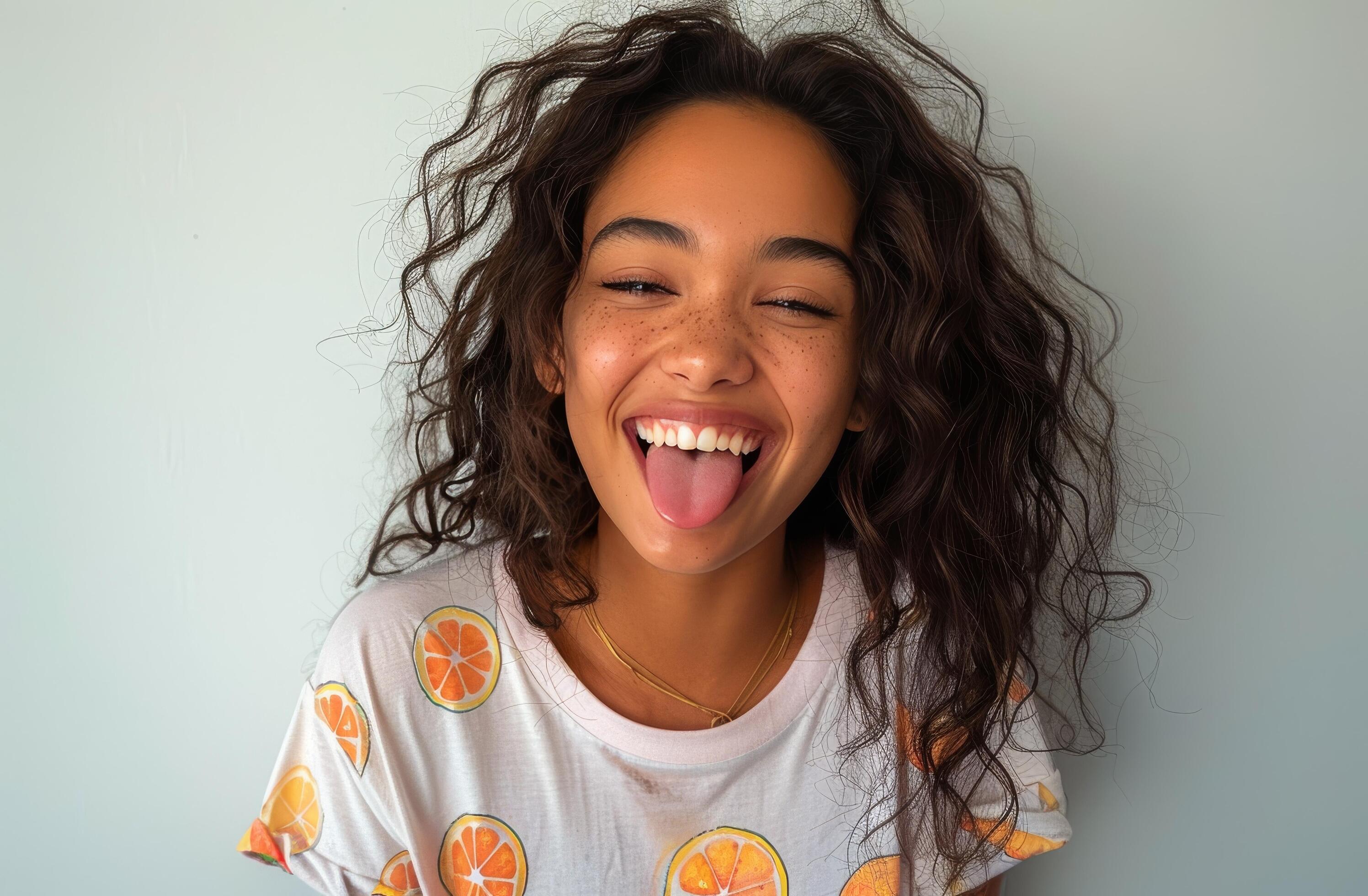 Young Woman With Curly Hair Smiles and Sticks Out Tongue Stock Free