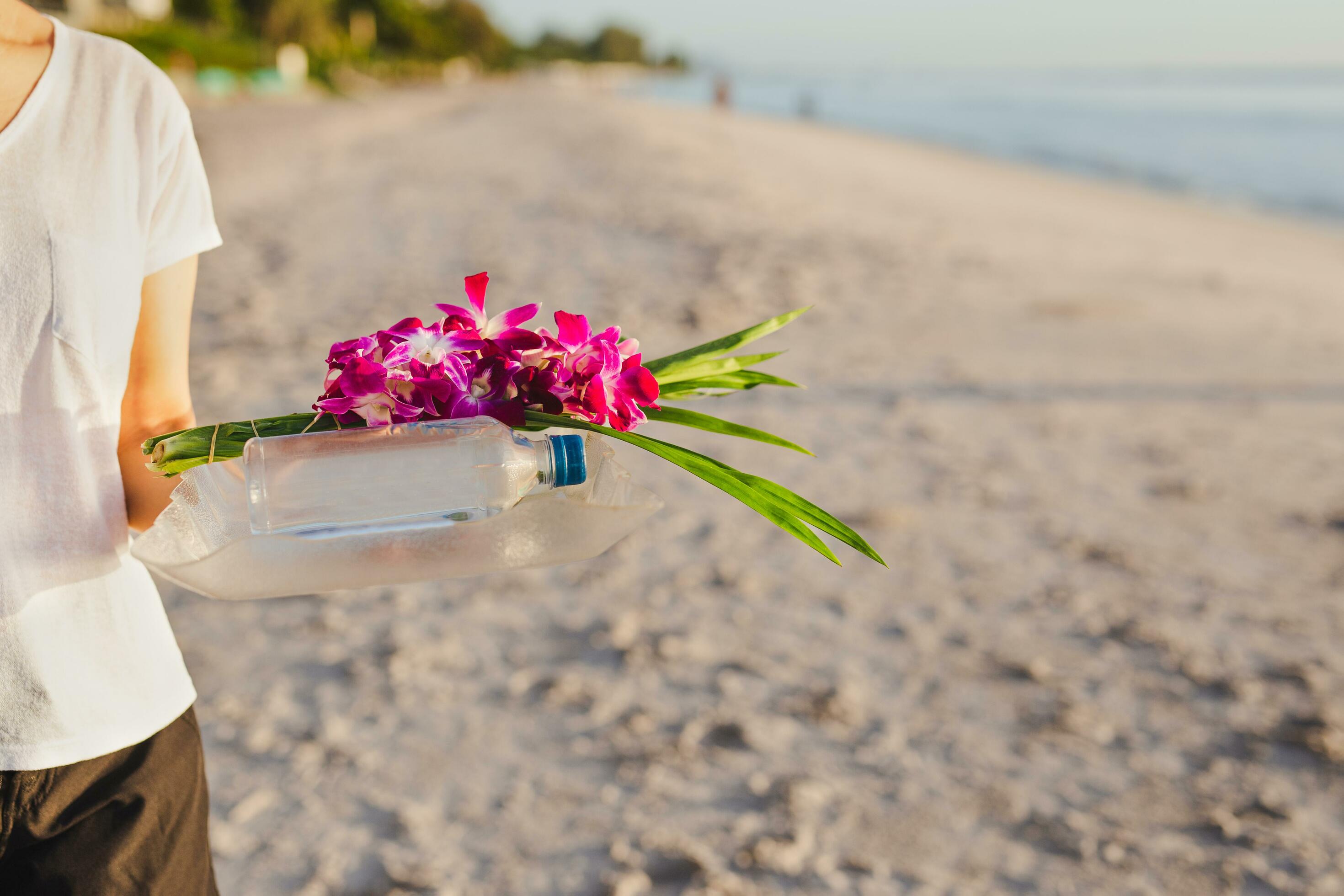 Woman hand holding orchid flowers and bottle of water on the beach. Stock Free