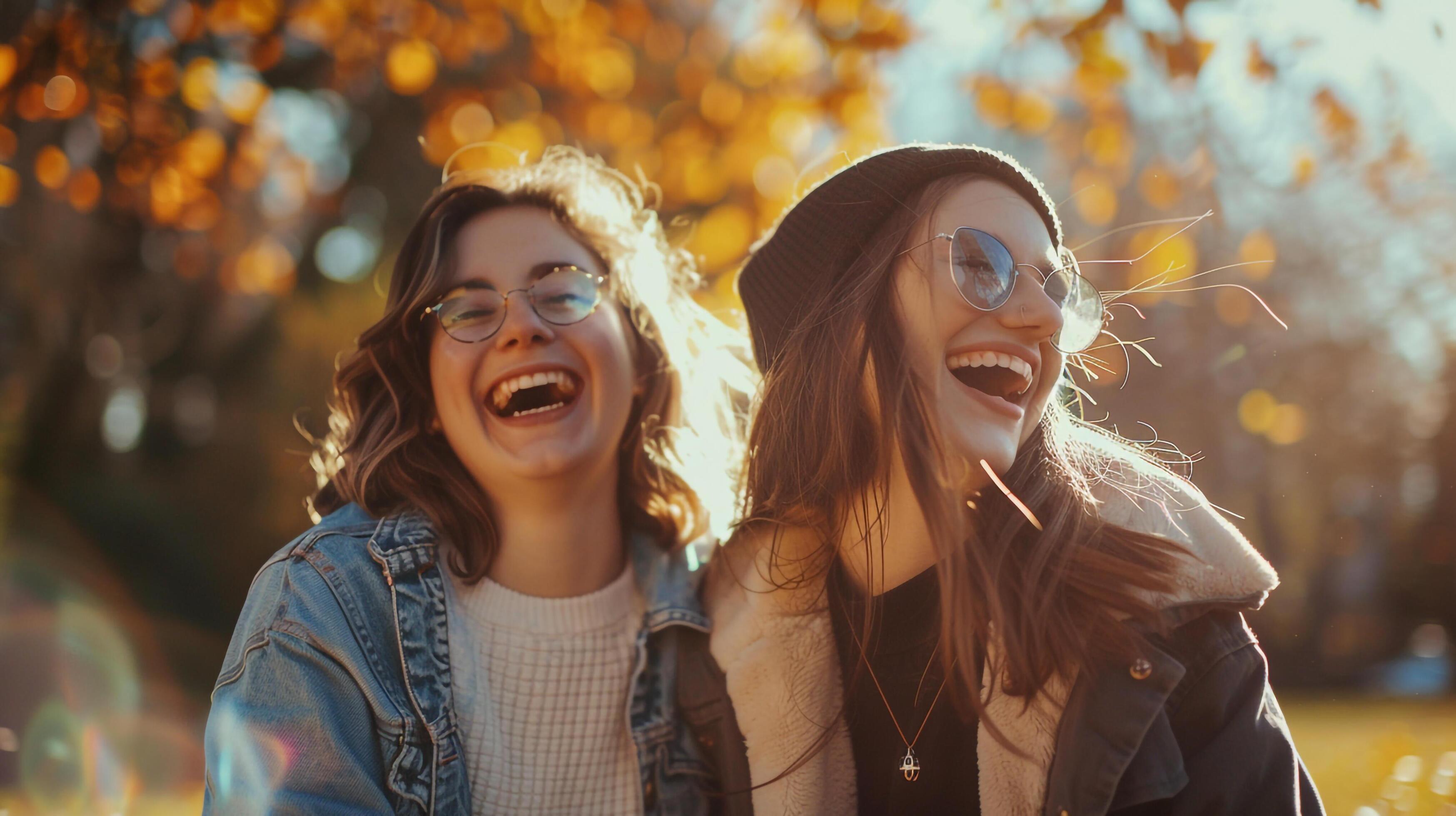 Two women laughing in a park with trees in the background Stock Free