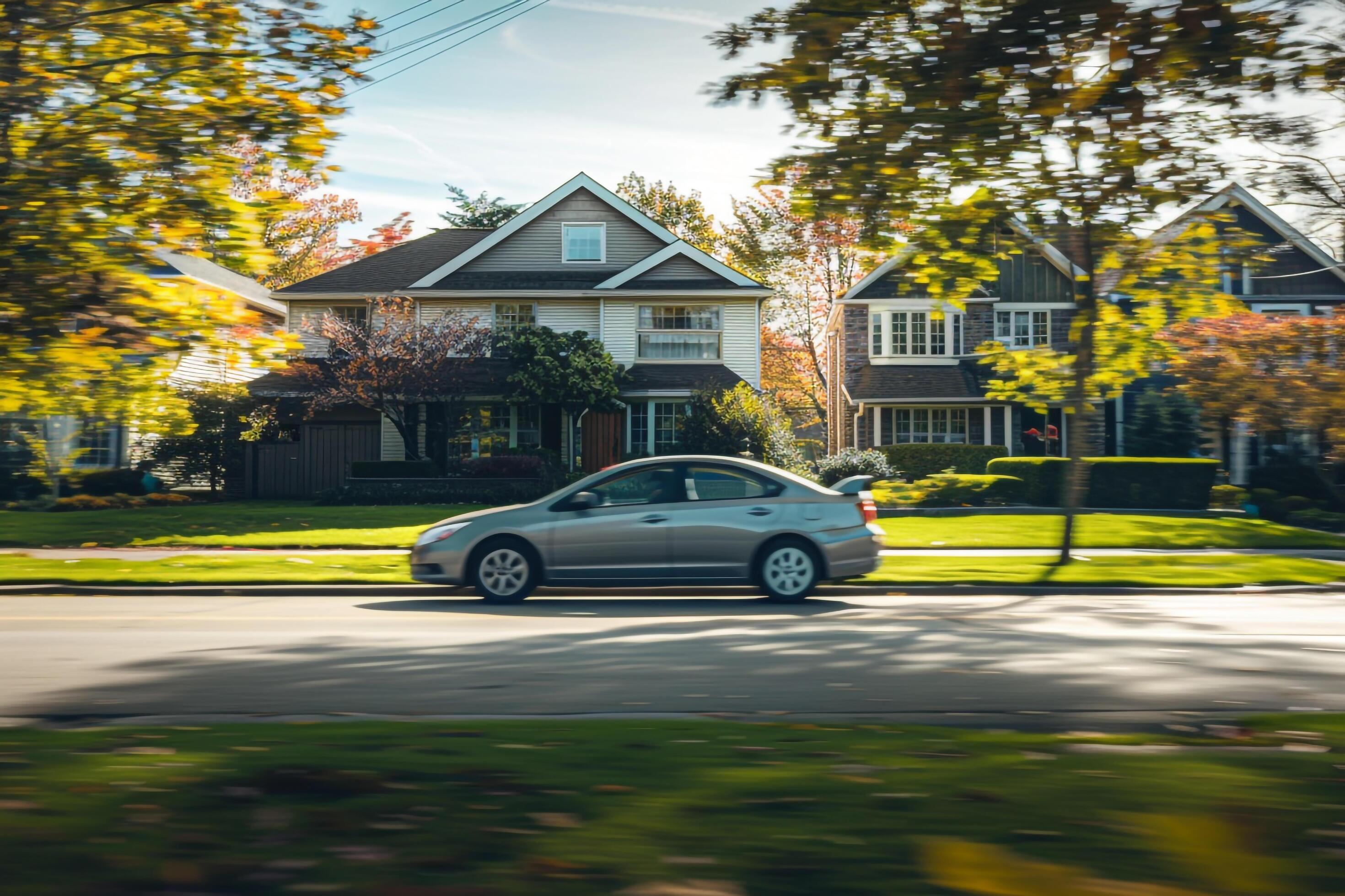 Subcompact sedan driving through suburban neighborhood with neatly trimmed lawns and family homes in the background Stock Free