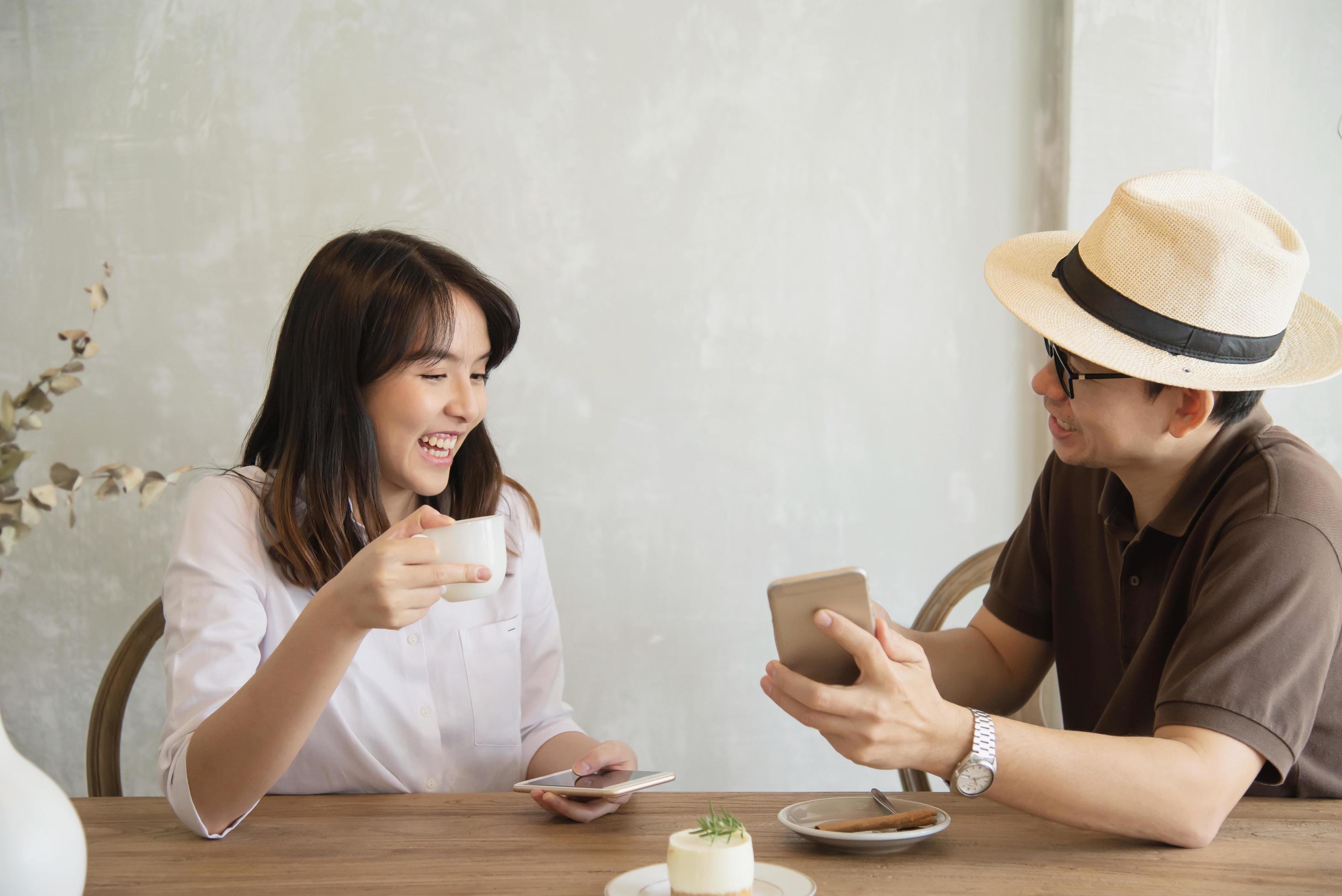 Casual man and woman talking happily while drink coffee and looking mobile phone – happy time lifestyle in coffee shop Stock Free