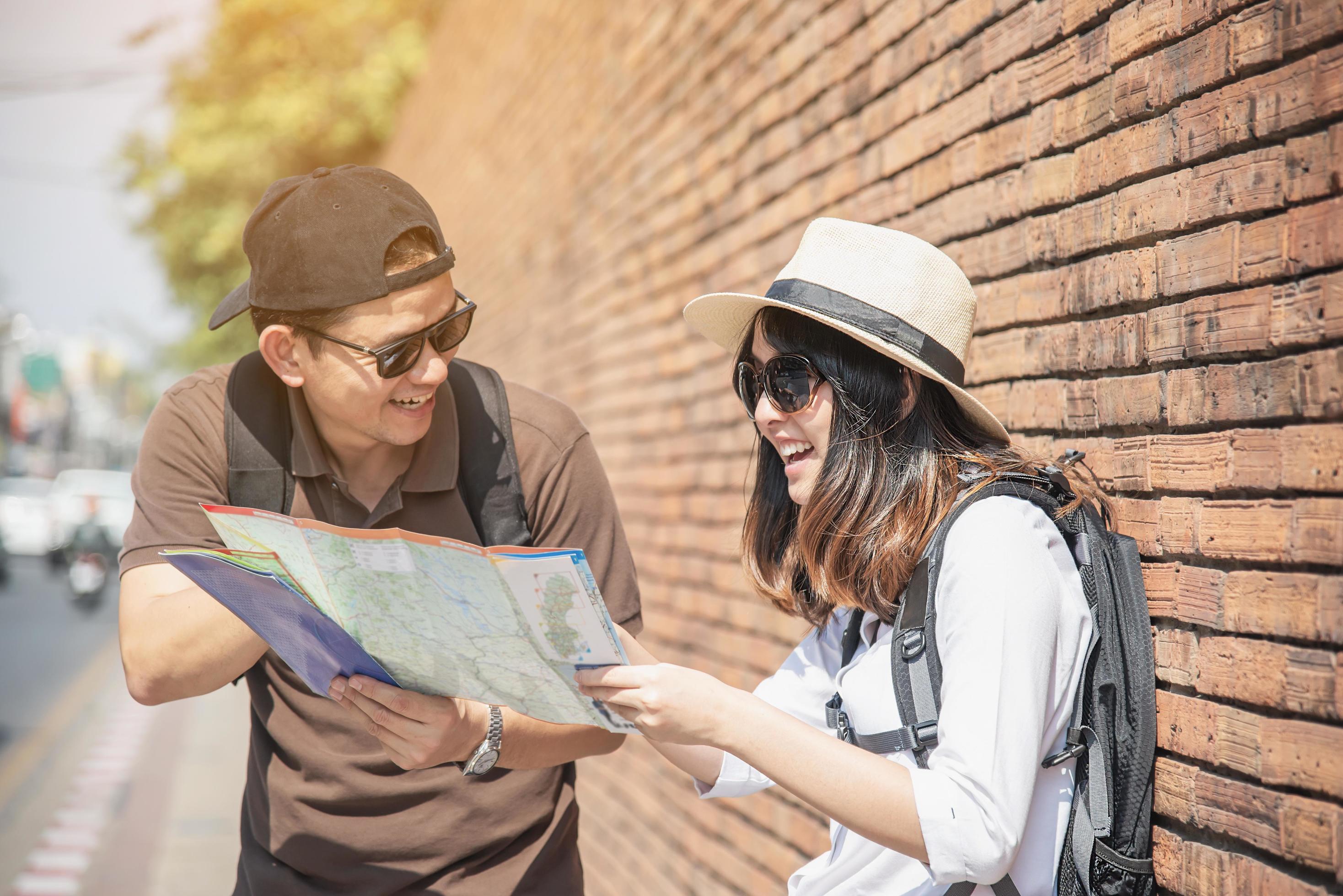 Asian backpack couple tourist holding city map crossing the road – travel people vacation lifestyle concept Stock Free