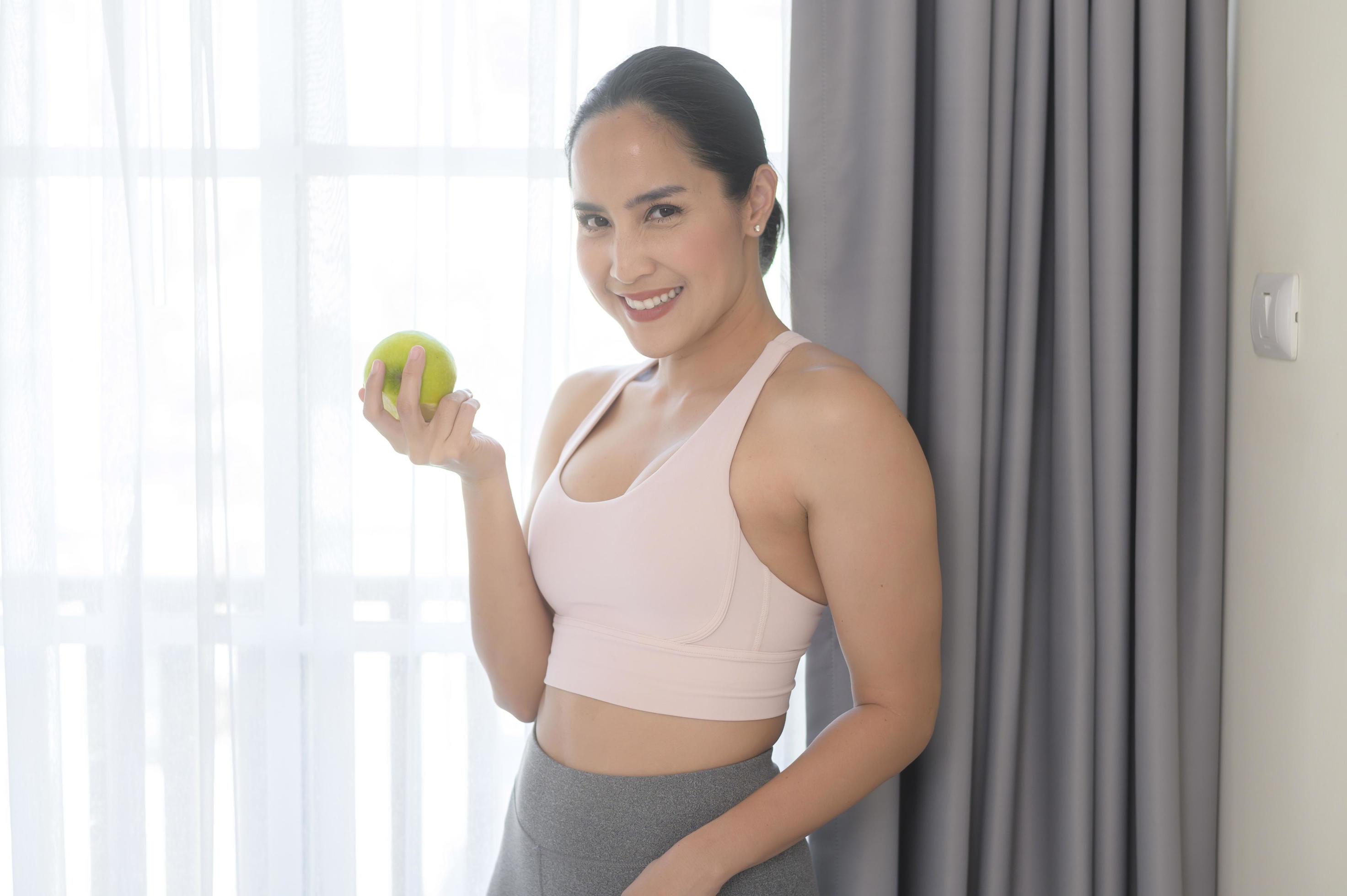 Fit young woman eating an apple after work out at home, sport and healthy lifestyle concept. Stock Free