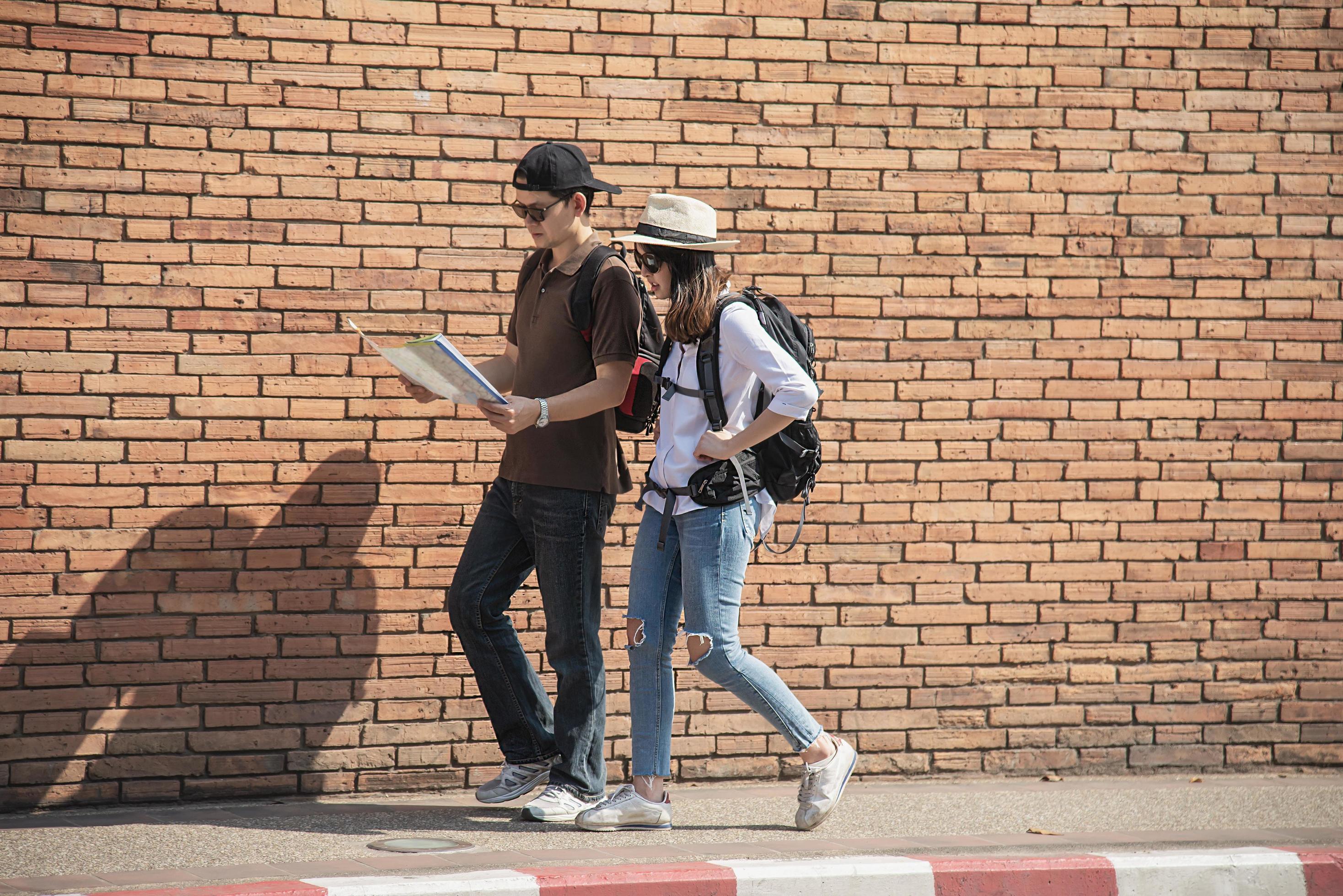 Asian backpack couple tourist holding city map crossing the road – travel people vacation lifestyle concept Stock Free