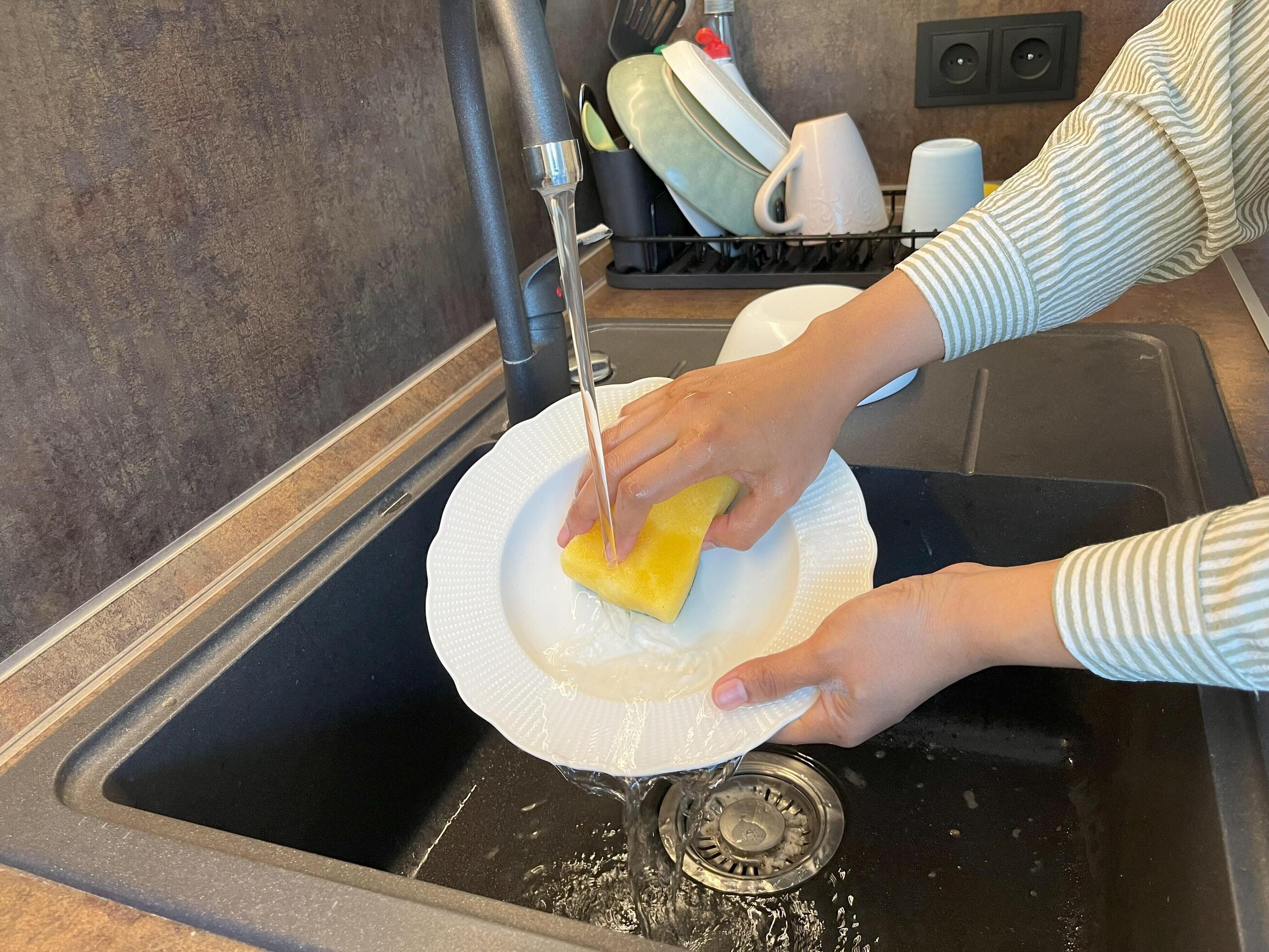 Close up of woman housewife is doing the dishes at home kitchen by using wash sponge and dishwashing soap. Clean the plate Stock Free