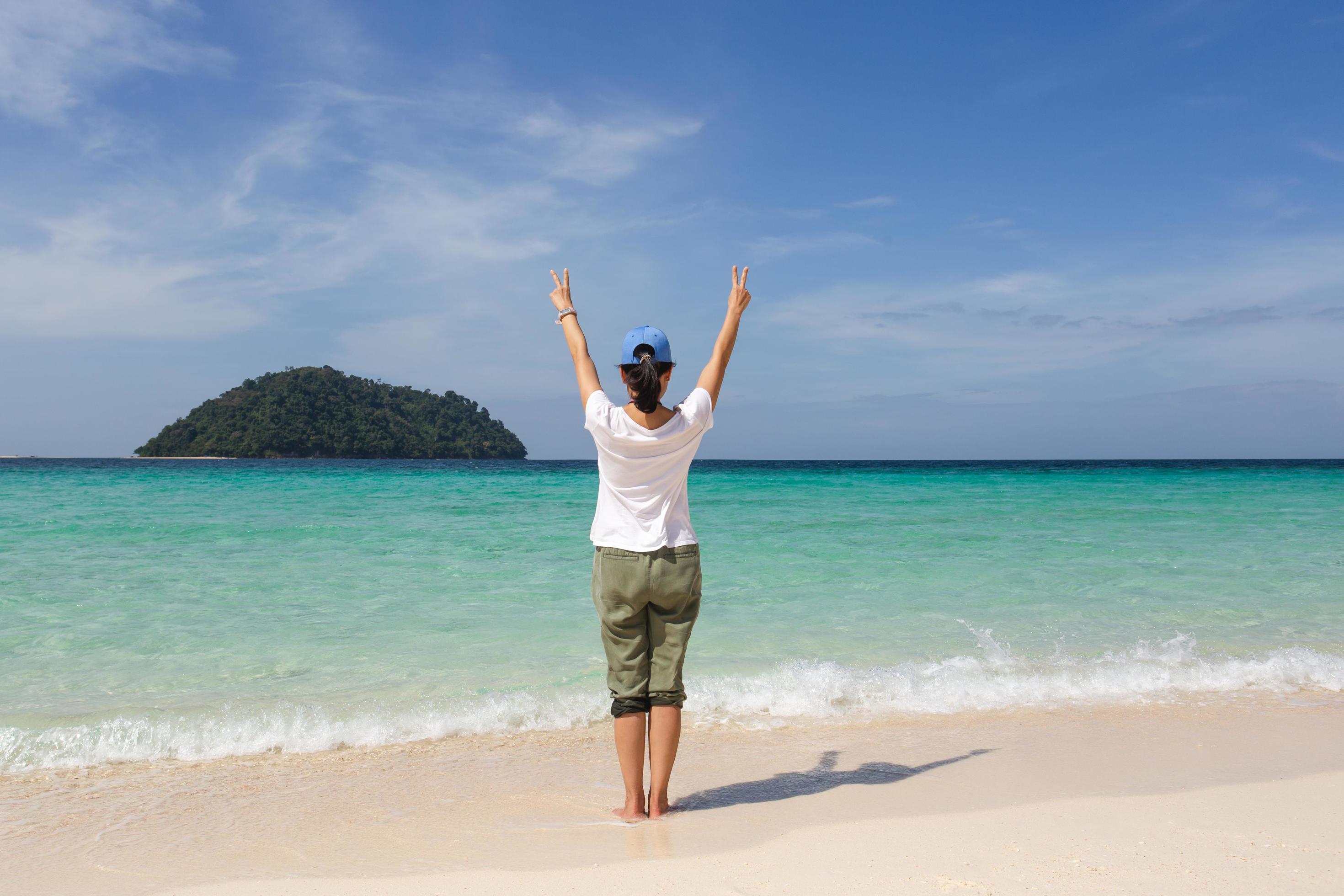 Back view of woman with hands raised up at the beach. Stock Free