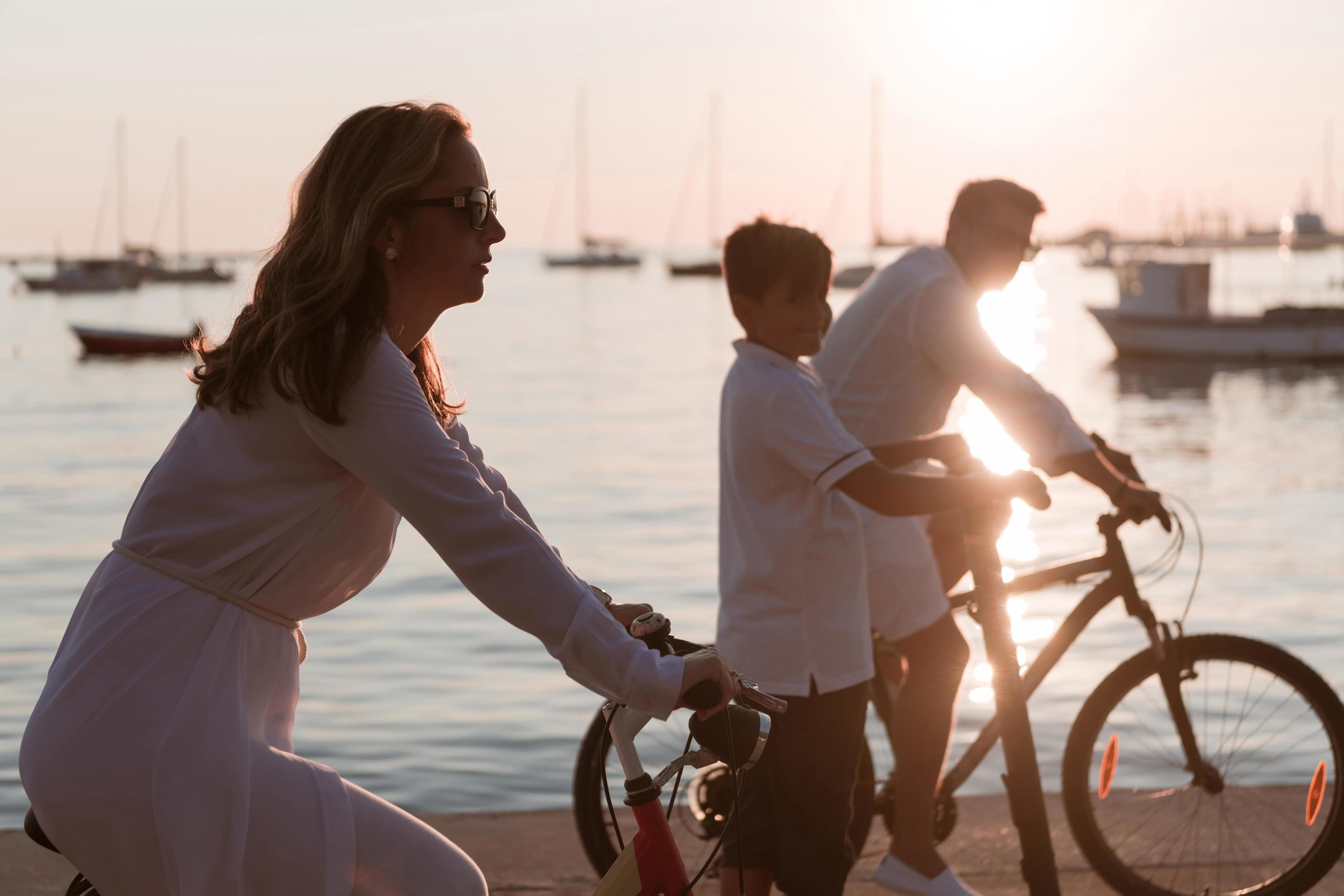 Happy family enjoying a beautiful morning by the sea together, parents riding a bike and their son riding an electric scooter. Selective focus Stock Free