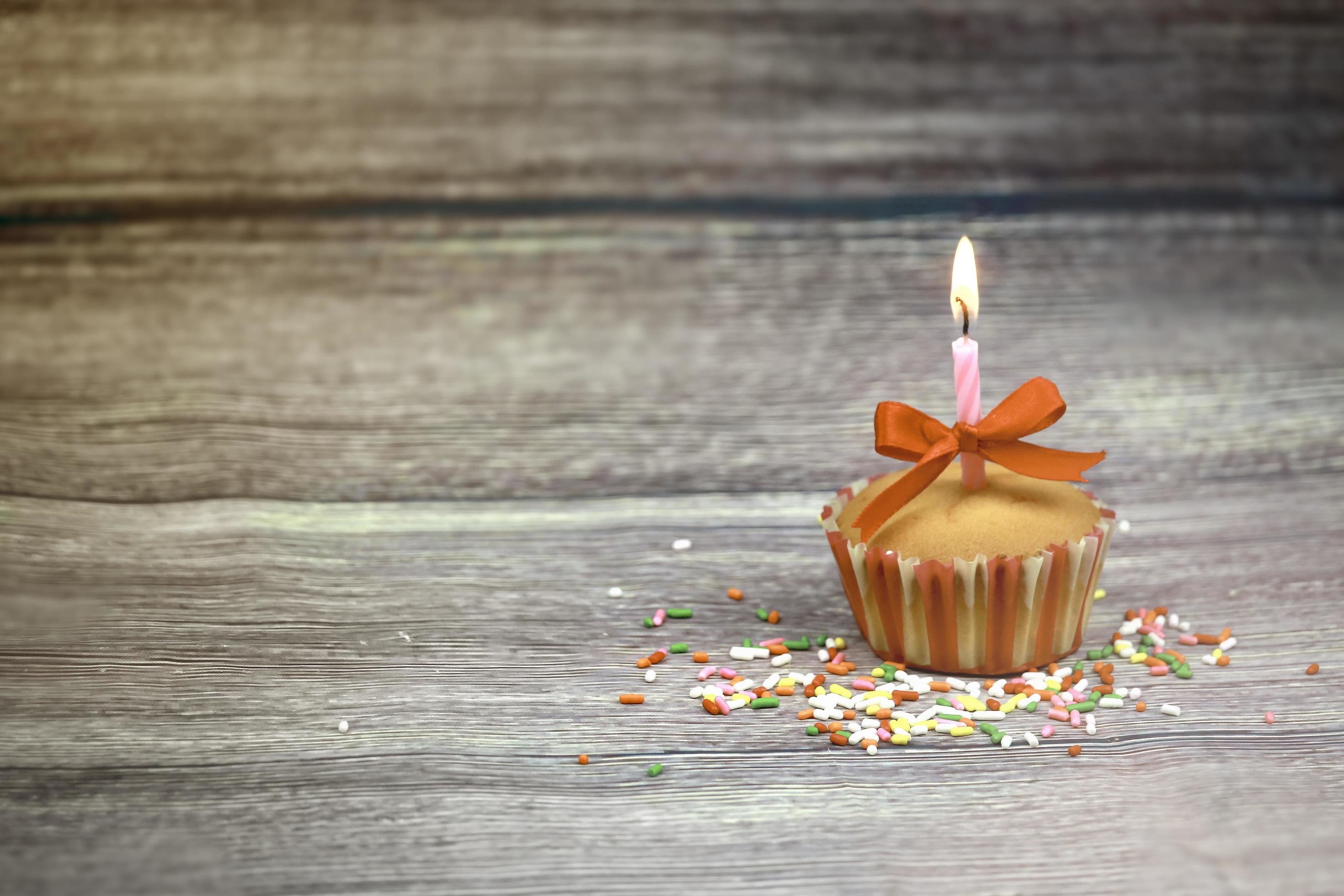 Happy birthday cupcake and bow candle on table on wooden background with copy space. Cute food happy birthday background concept Stock Free