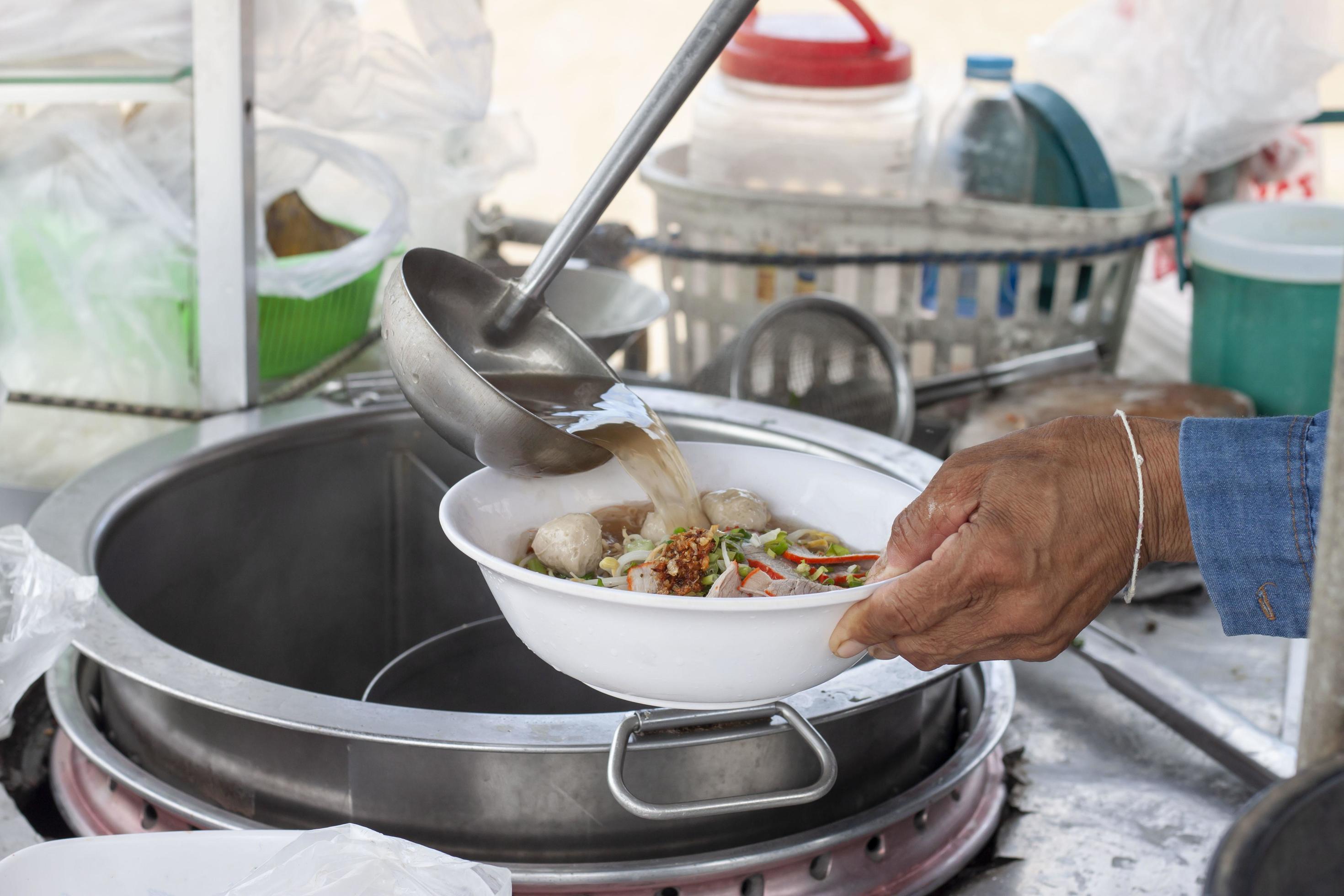 Hand of Asian Chef cooking noodle soup with meat ball in local restaurant, Thailand street food. Stock Free