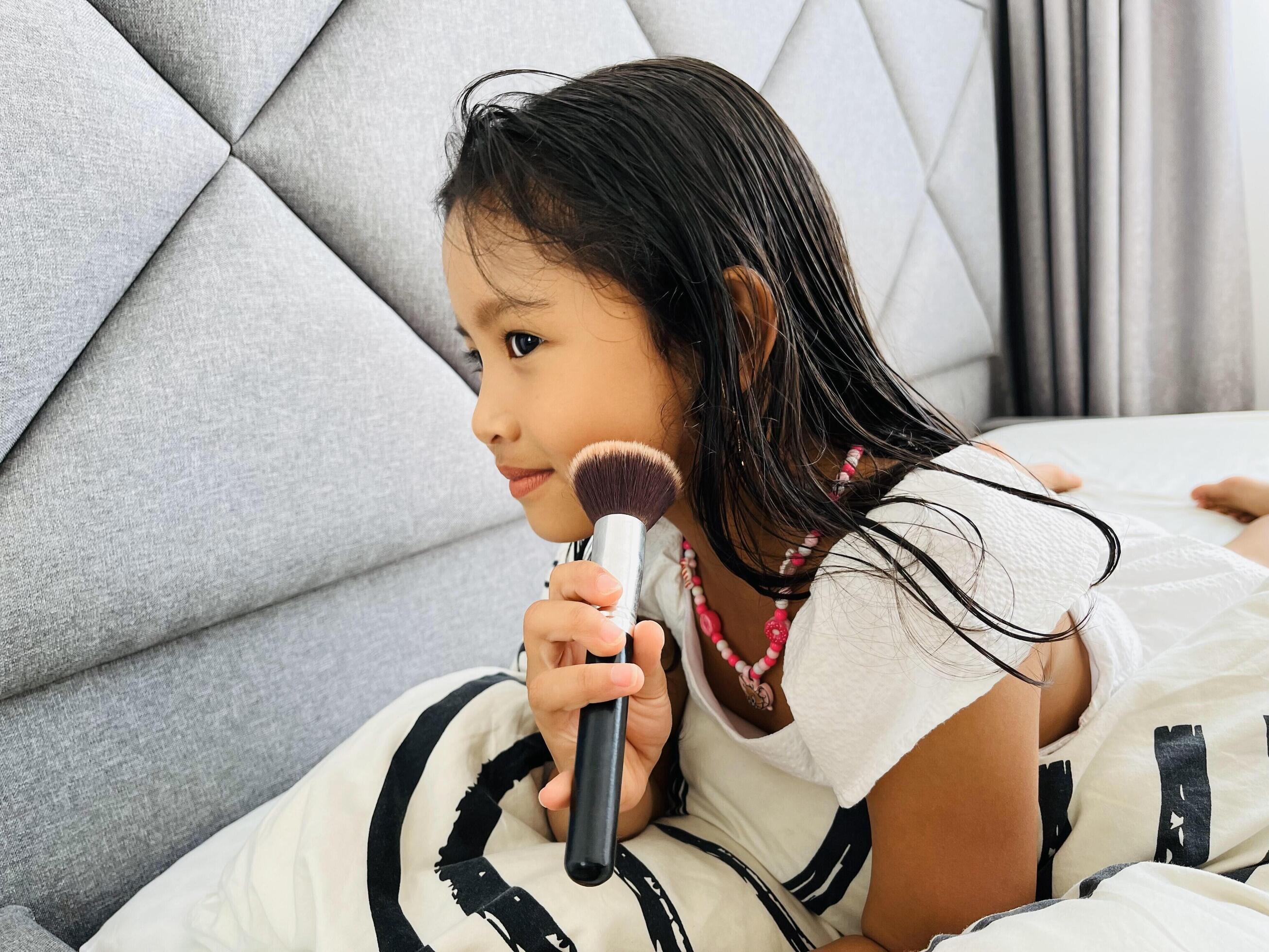 Beautiful little Asian girl holding blush brush. A five year old in beautiful white dresses preening in the bed Stock Free