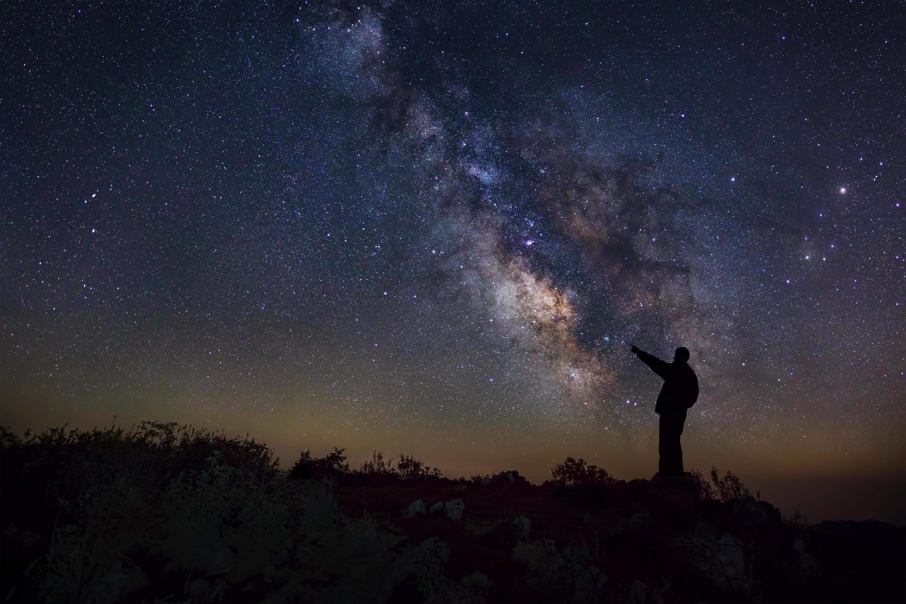 A Man is standing next to the milky way galaxy pointing on a bright star, Long exposure photograph, with grain Stock Free