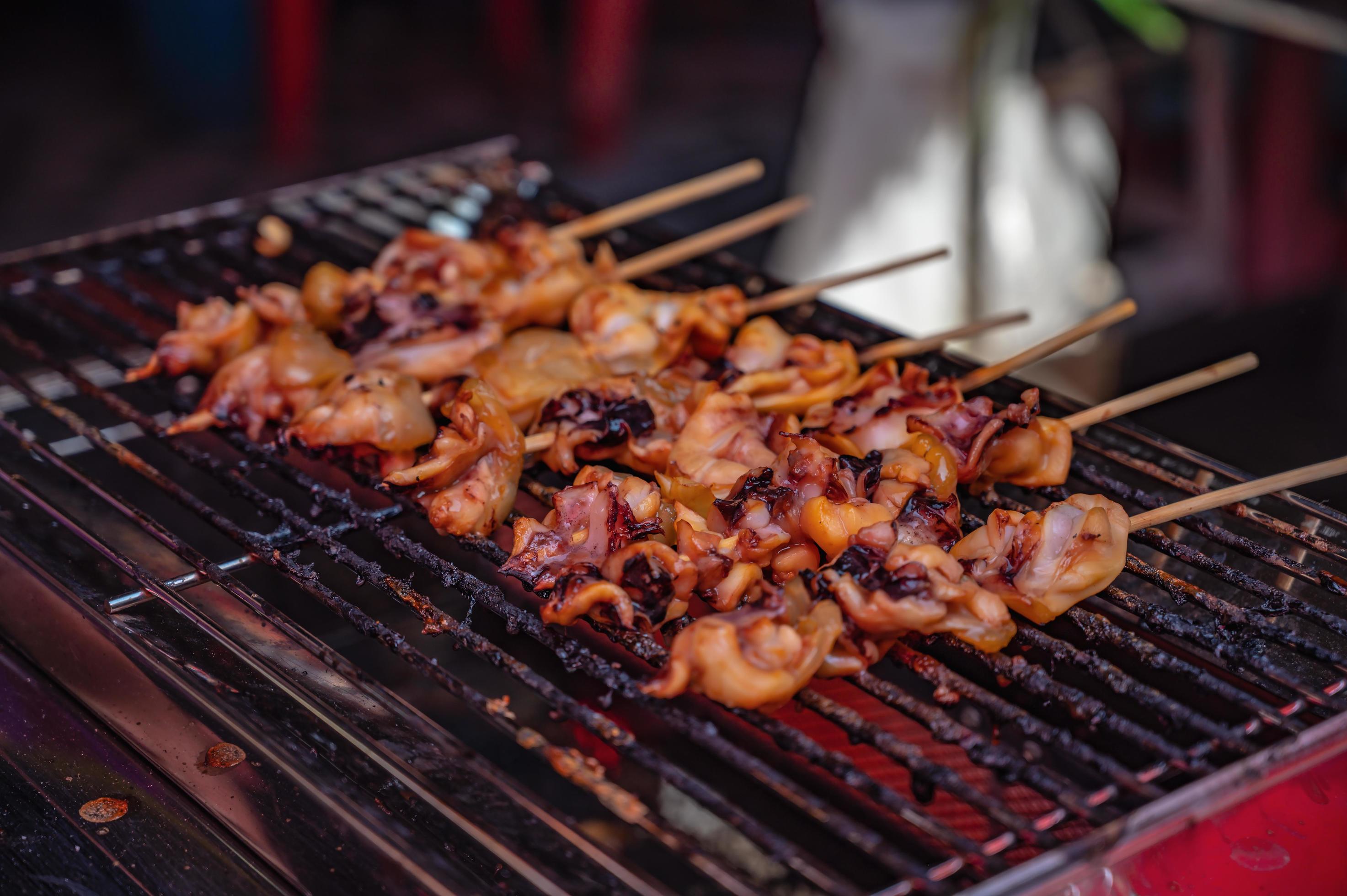 Close up raw squid meat skewer on banana leaf in the fresh market of thailand with spicy seafood sauce.Thailand street food Stock Free