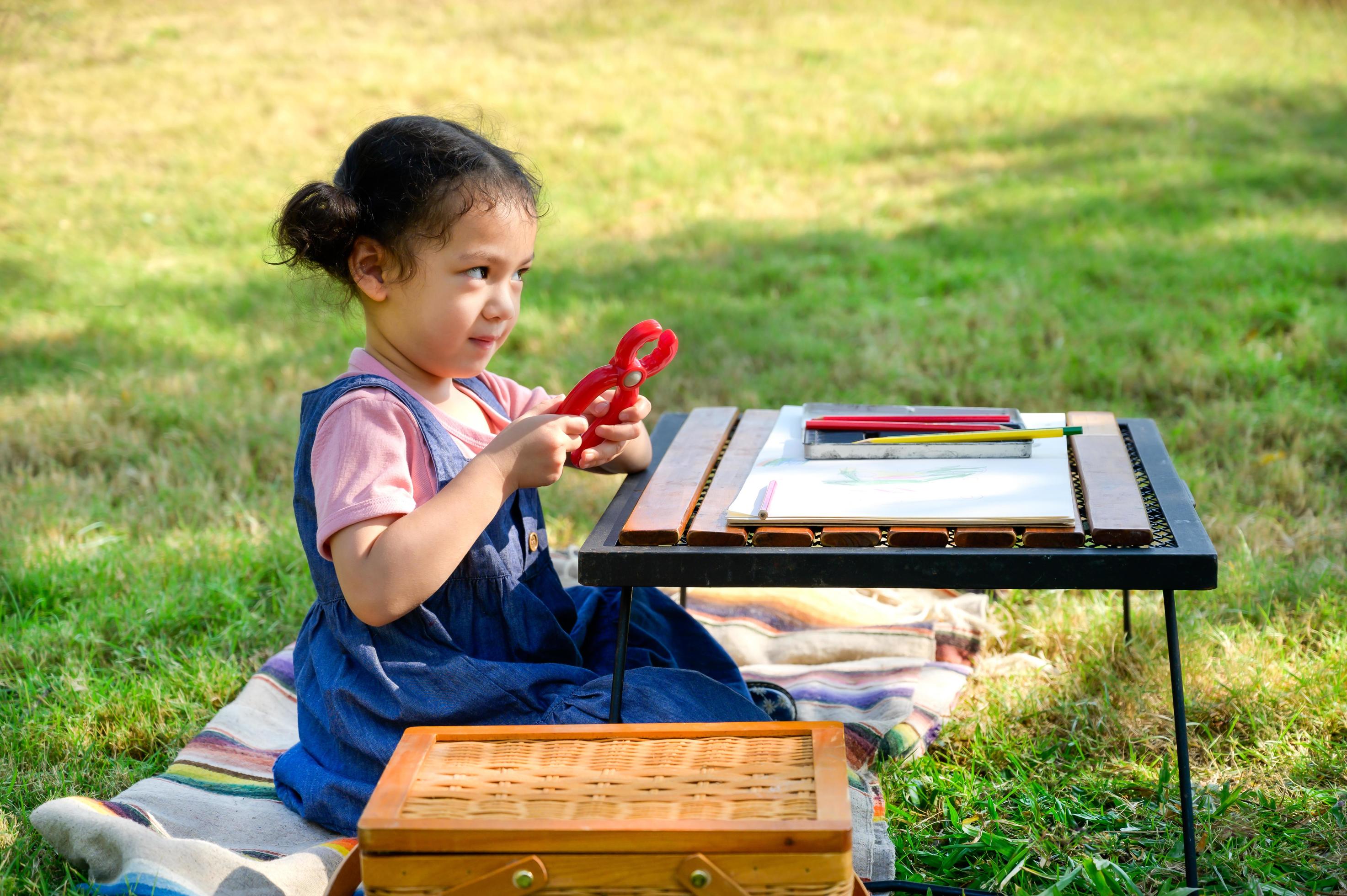 A little girl is sitting on the cloth and playing a toy befor painted on the paper Stock Free