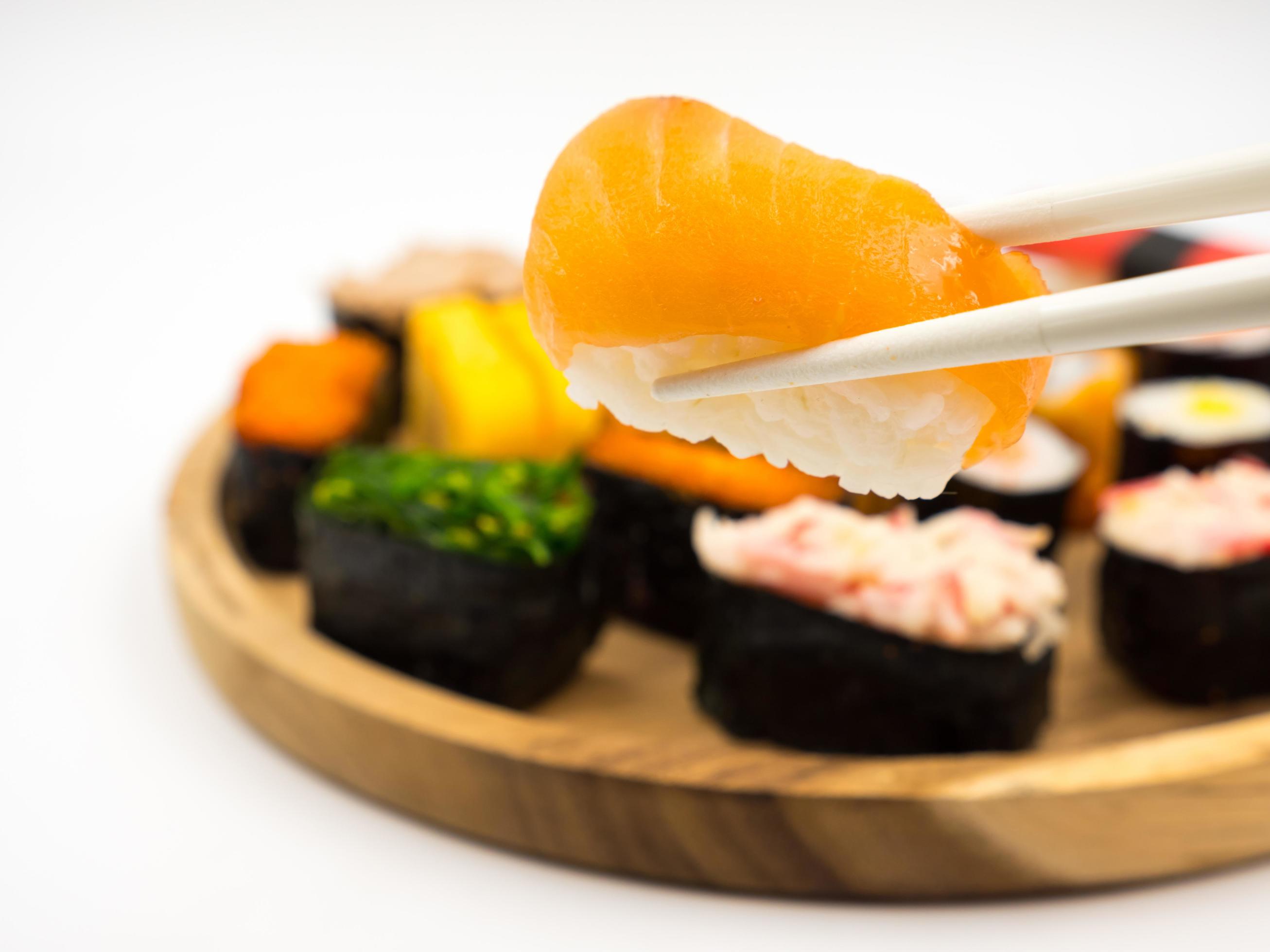 Hand holding sushi with chopsticks, Sushi set on wooden plate background, Japanese food. Stock Free