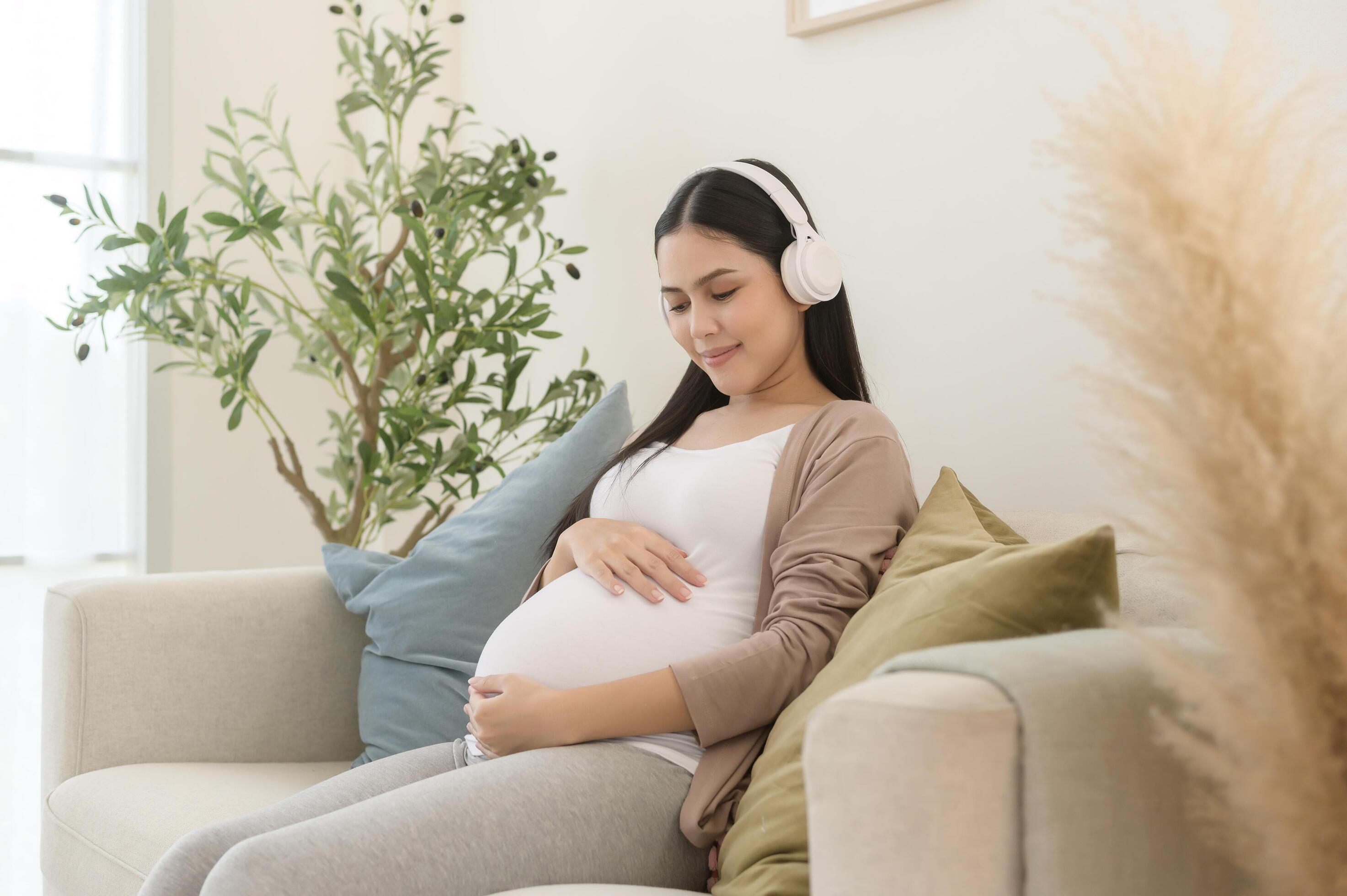 Happy pregnant woman with headphones listening to mozart music and lying on sofa, pregnancy concept Stock Free