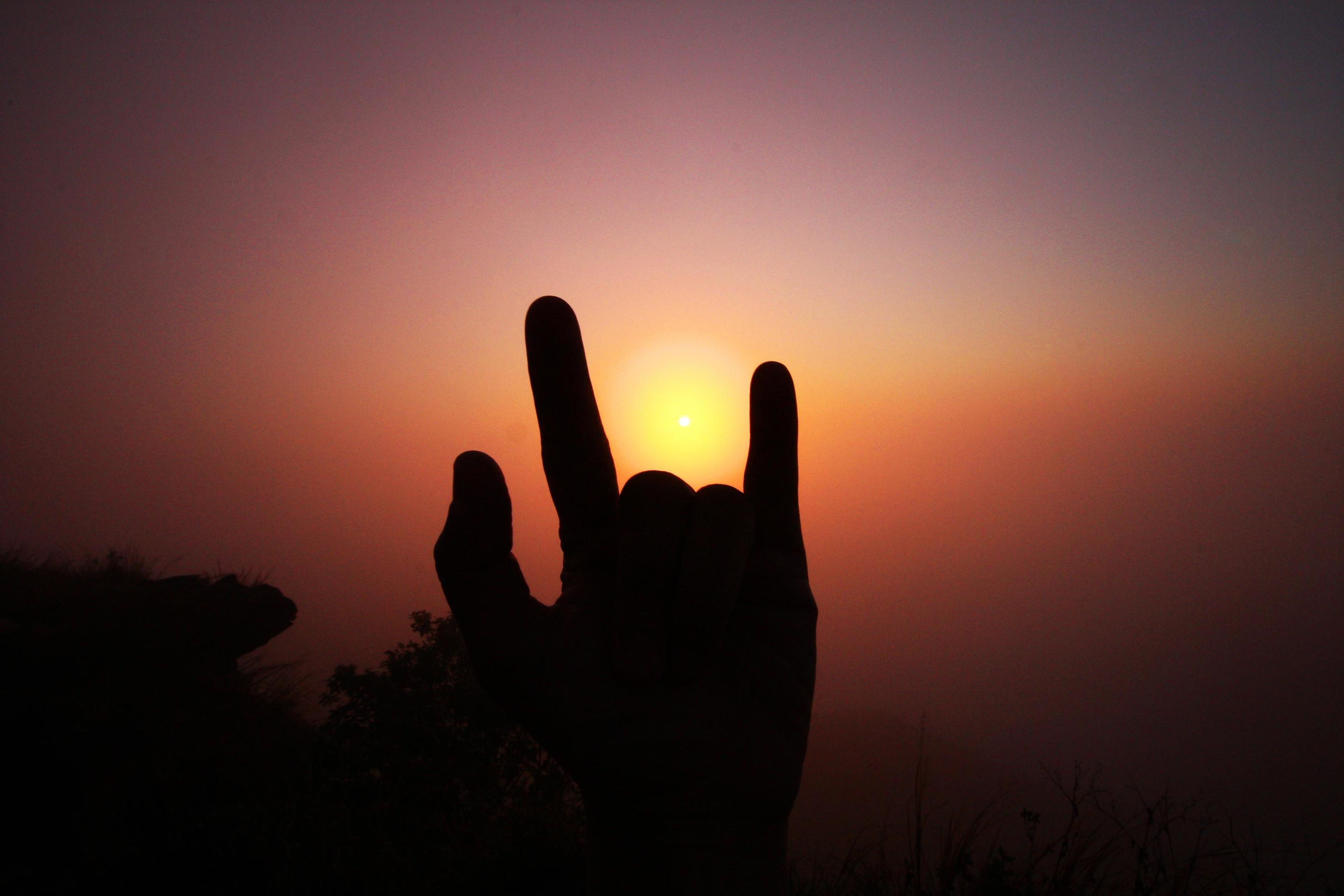 Beautiful silhouette of fingers and hand with valley of mountain in foggy and mist of sunrise shining on the sky Stock Free