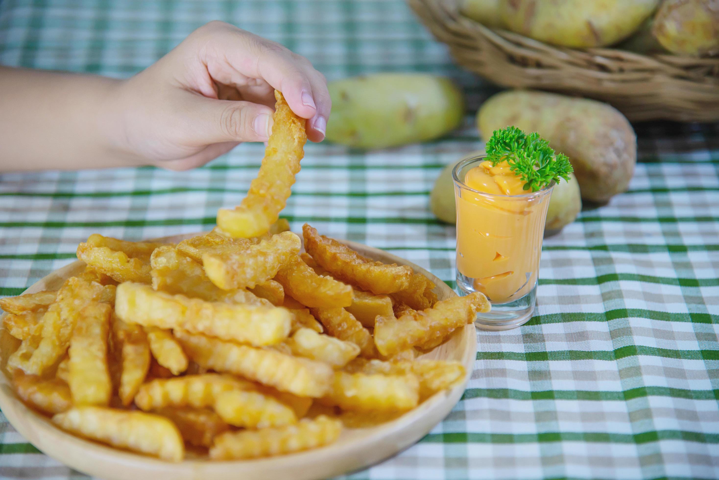 Hand holding delicious fried potato on wooden plate with dipped sauce – traditional fast food concept Stock Free