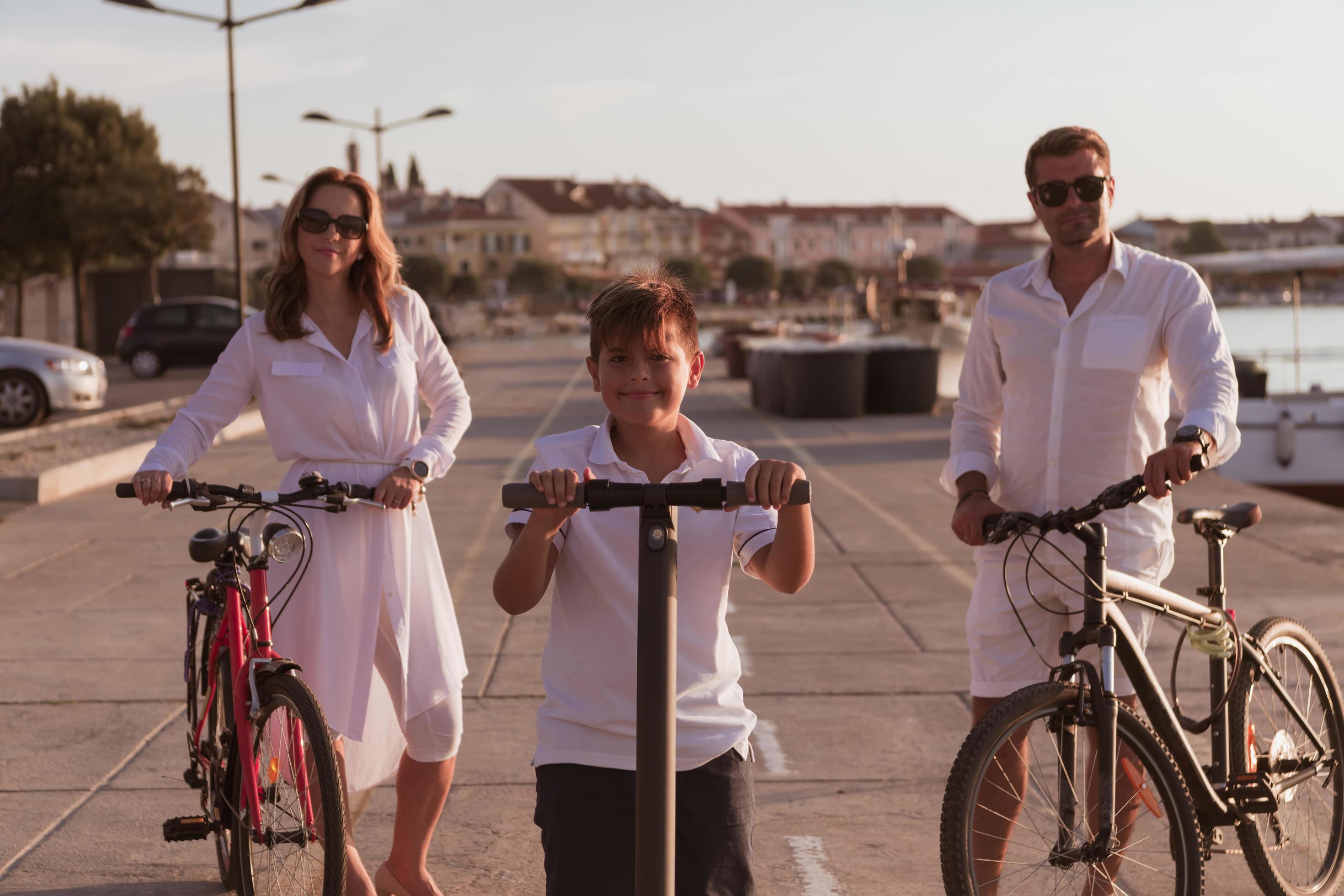 Happy family enjoying a beautiful morning by the sea together, parents riding a bike and their son riding an electric scooter. Selective focus Stock Free