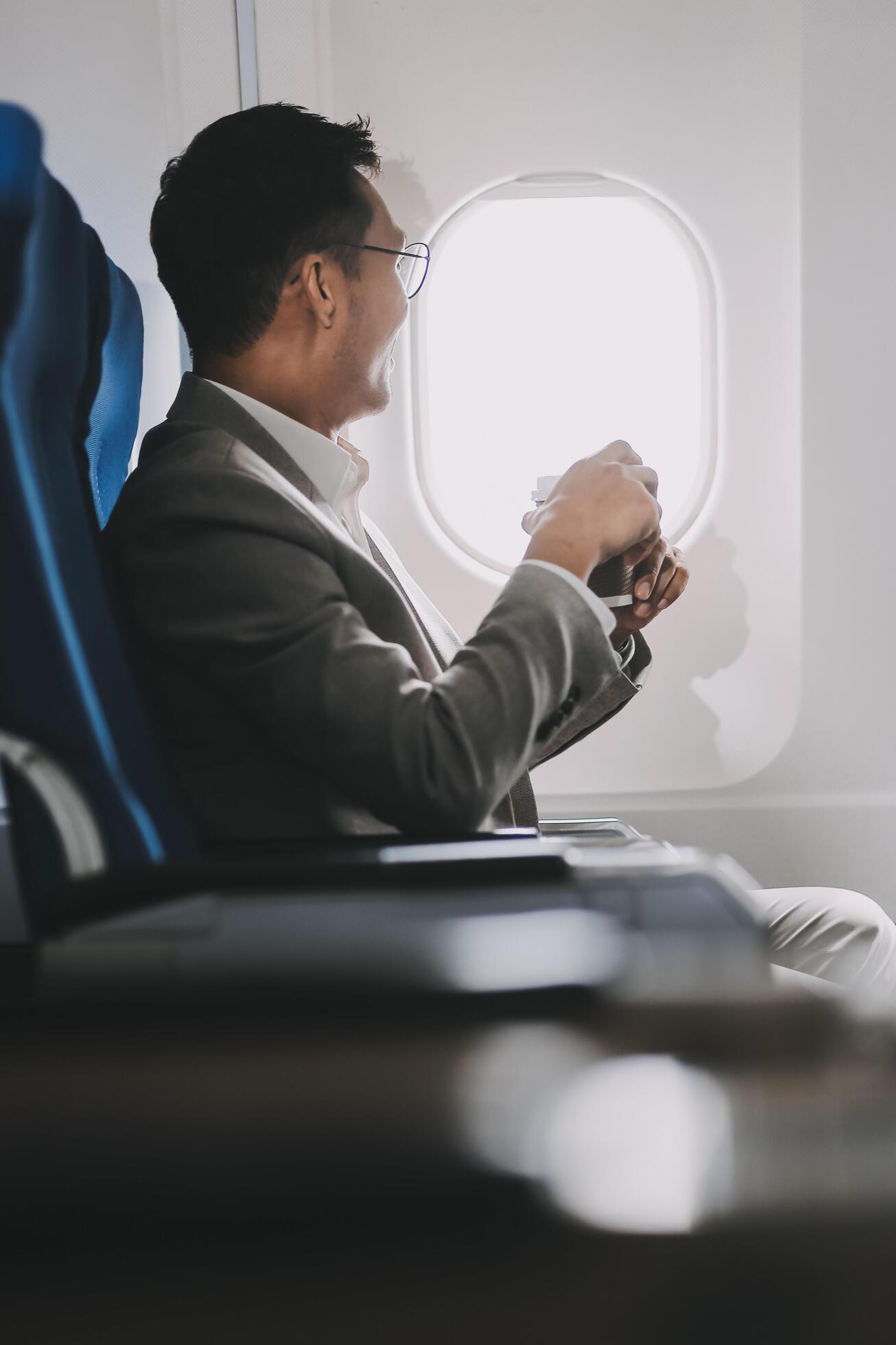 Asian businessman enjoying enjoys a coffee comfortable flight while sitting in the airplane cabin, Passengers near the window. Stock Free