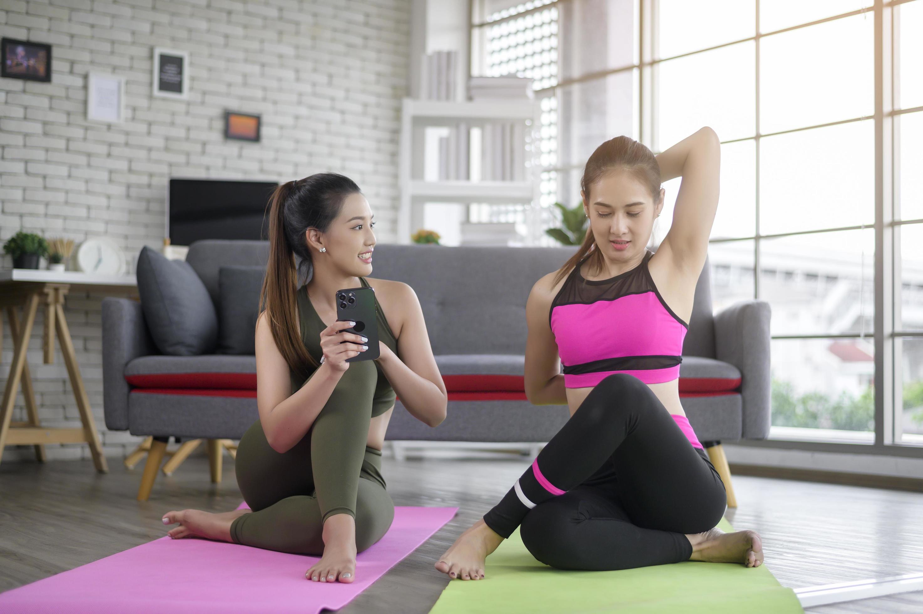 Young friend women practicing yoga at home unsing smart phone via online class with professional instructor, sport and healthy lifestyle concept. Stock Free