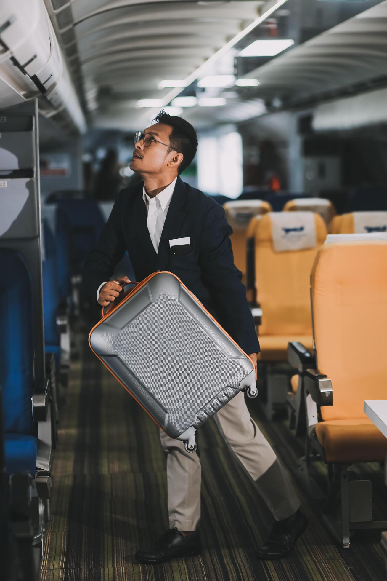 Handsome Asian male passenger takes his carry-on luggage out of the overhead locker after landing at his destination. transportation concept Stock Free