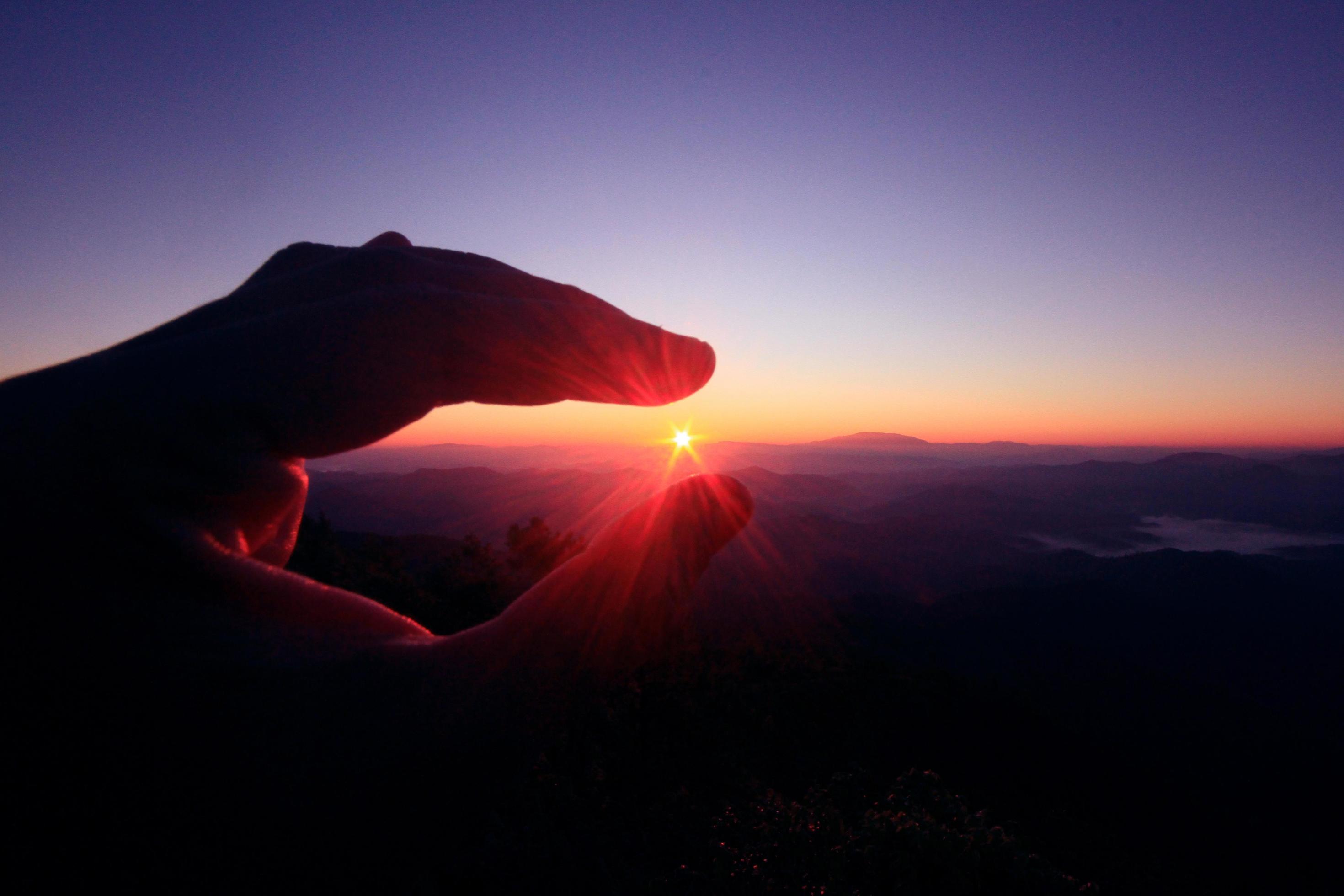 Woman fingers pick beautiful sun in natural twilight of sunset on the mountain Stock Free