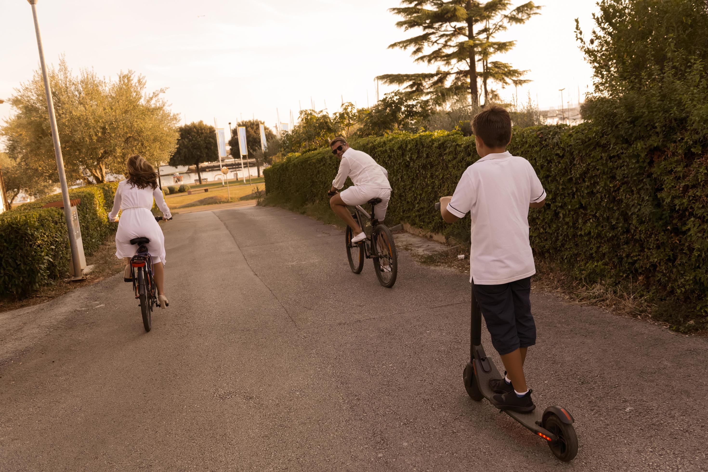 Happy family enjoying a beautiful morning together, parents riding a bike and their son riding an electric scooter. Selective focus Stock Free