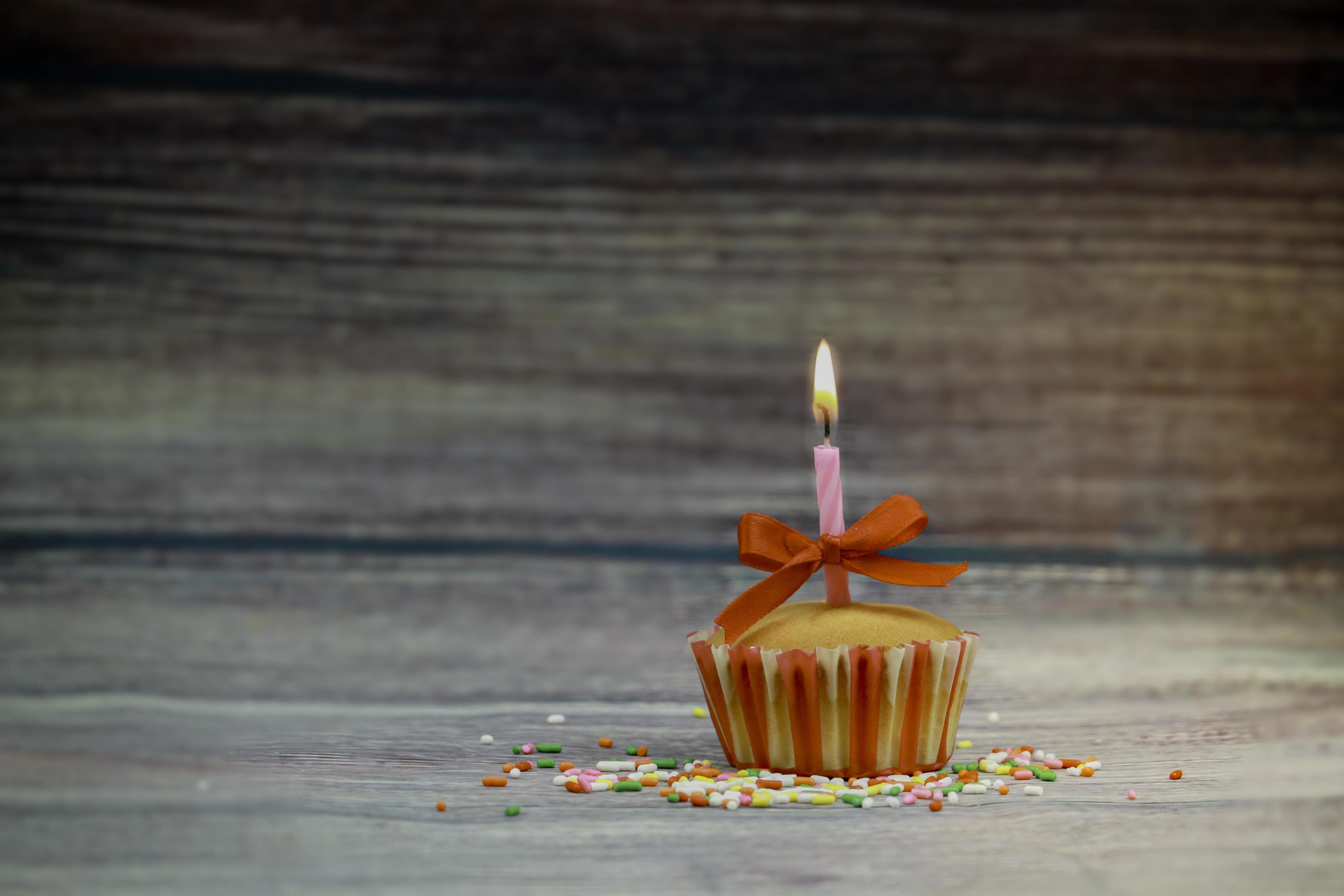 Happy birthday cupcake and bow candle on table on wooden background with copy space. Cute food happy birthday background concept Stock Free