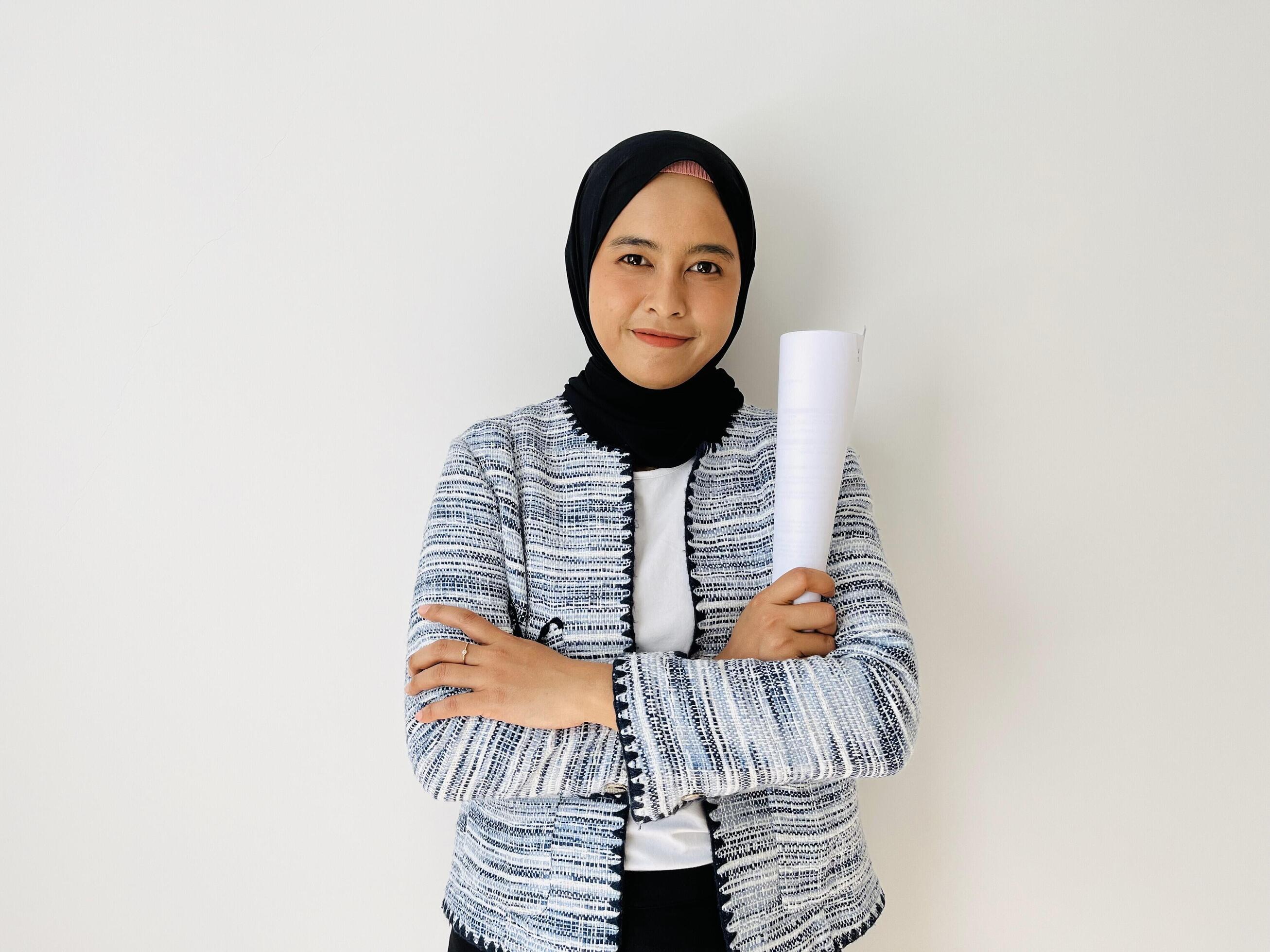 A young Asian Muslim woman holds rolled up paper and crosses her arms. Successful young entrepreneur Stock Free