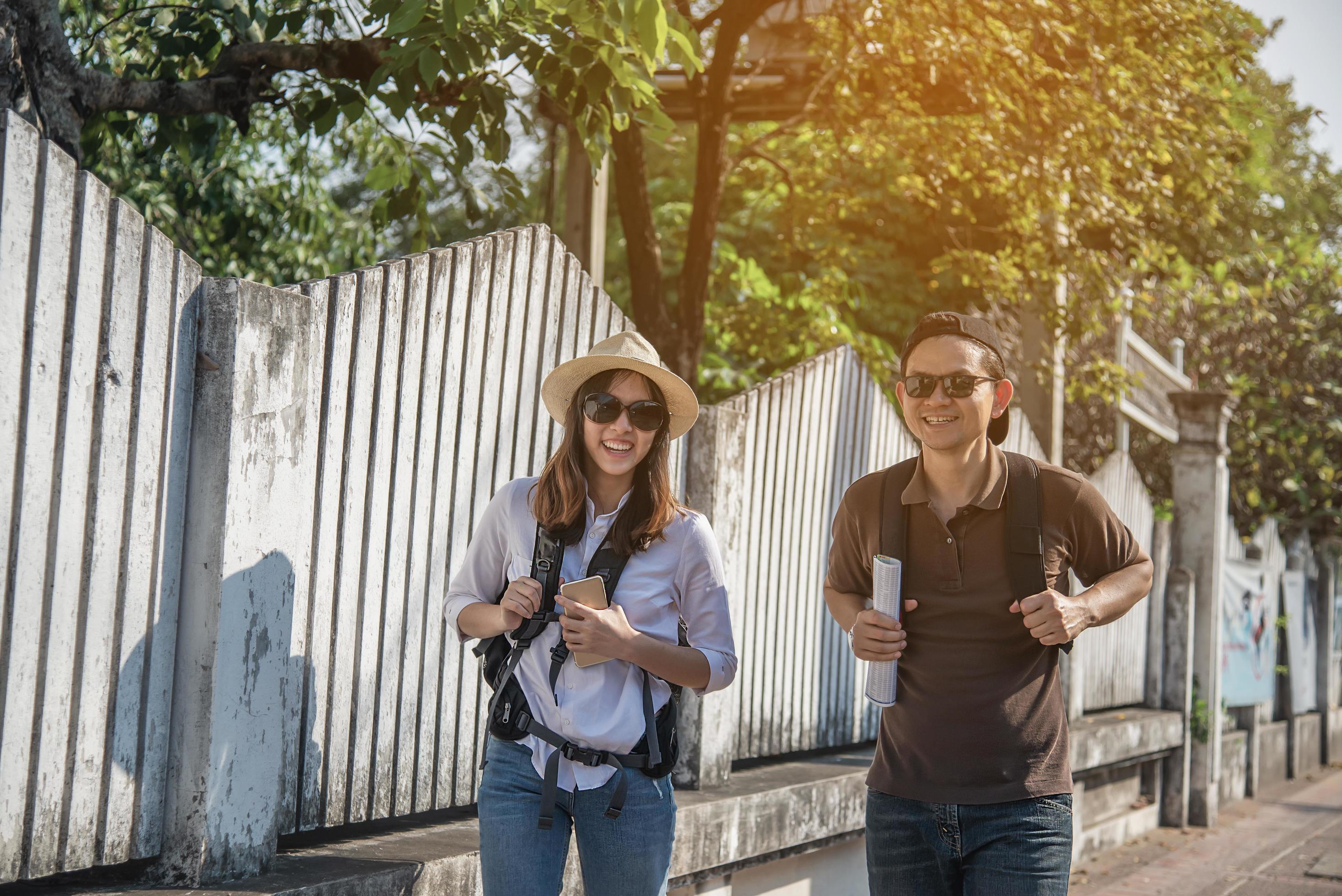 Asian backpack couple tourist holding city map crossing the road – travel people vacation lifestyle concept Stock Free