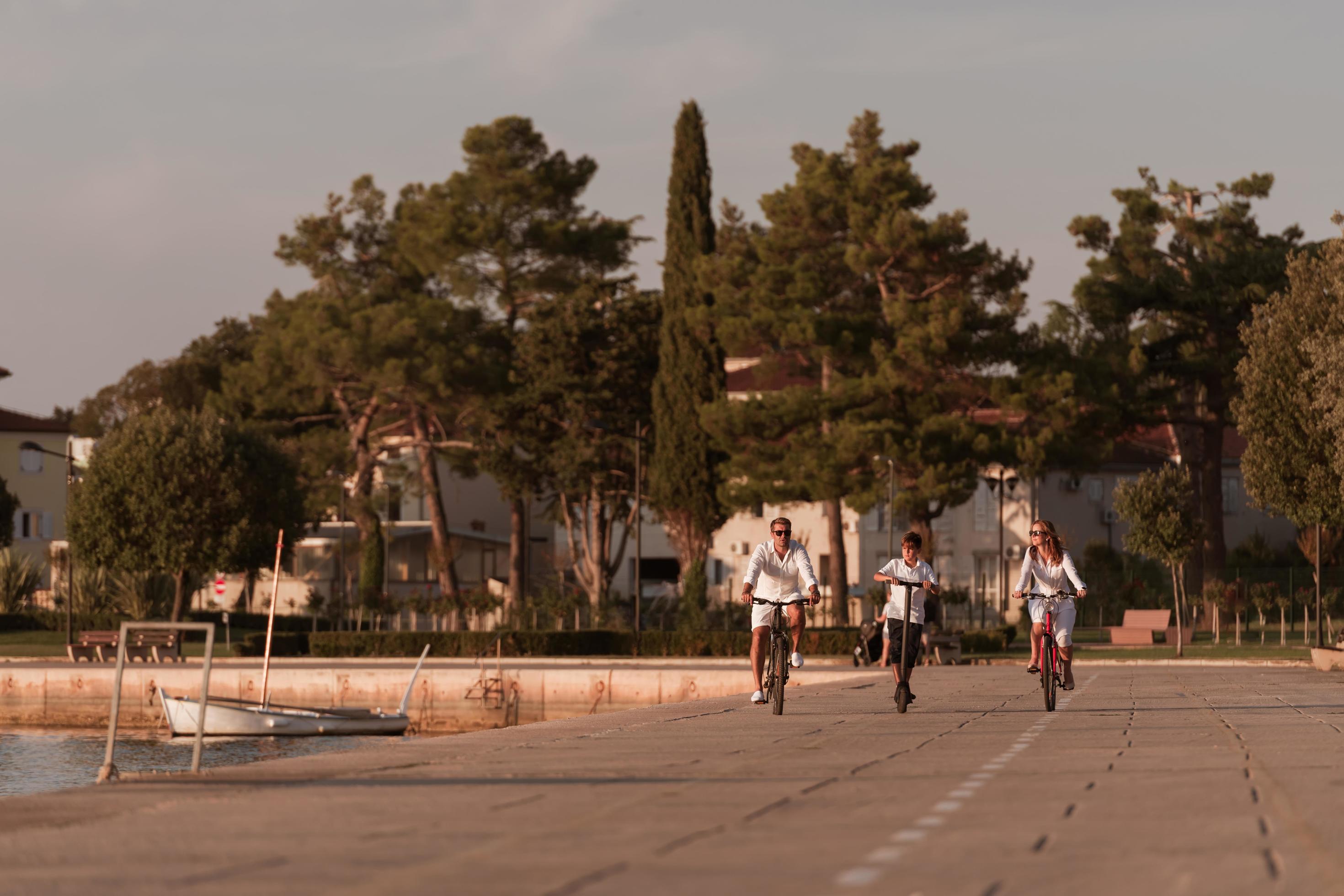 Happy family enjoying a beautiful morning by the sea together, parents riding a bike and their son riding an electric scooter. Selective focus Stock Free