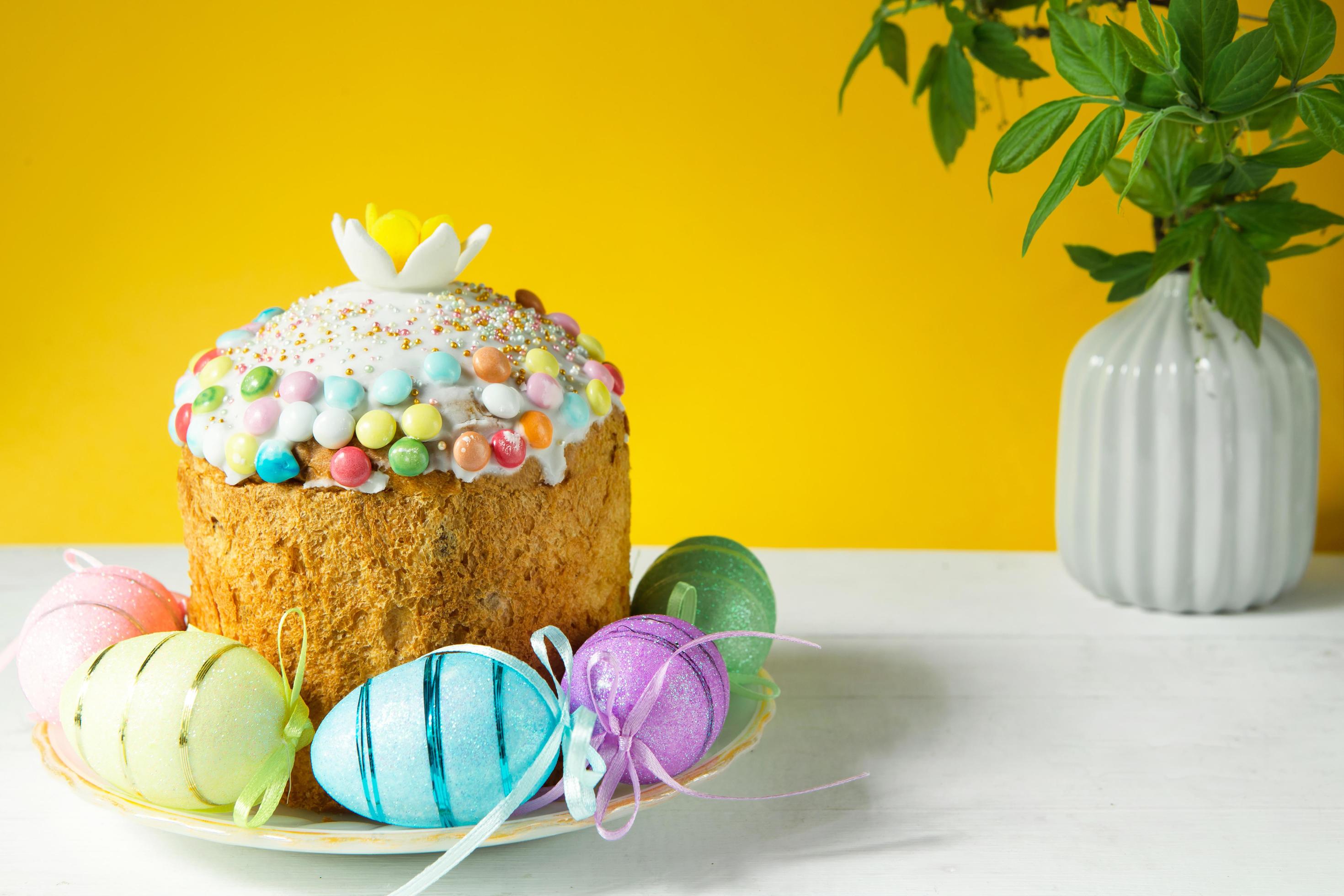 Easter cake with painted eggs on a platter in a white table. Traditional festive food. Yellow background Stock Free