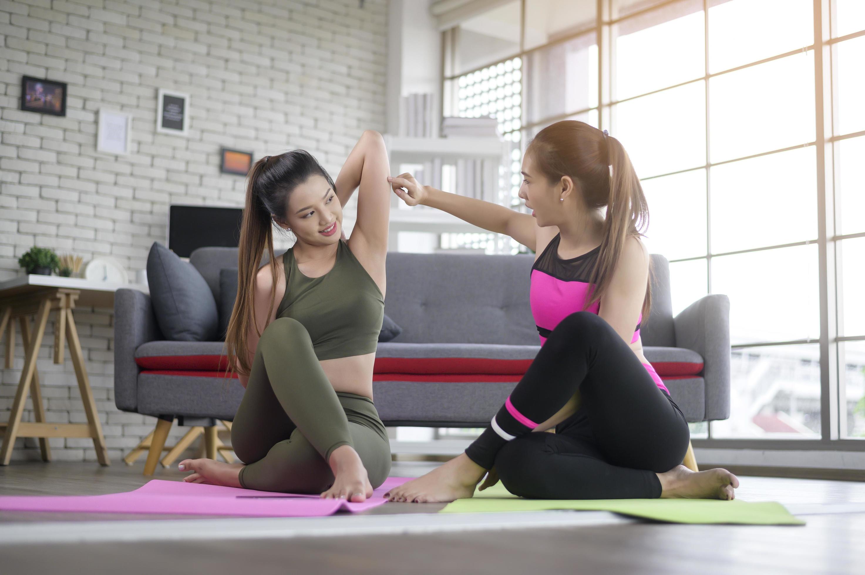 Young friend women practicing yoga at home unsing smart phone via online class with professional instructor, sport and healthy lifestyle concept. Stock Free