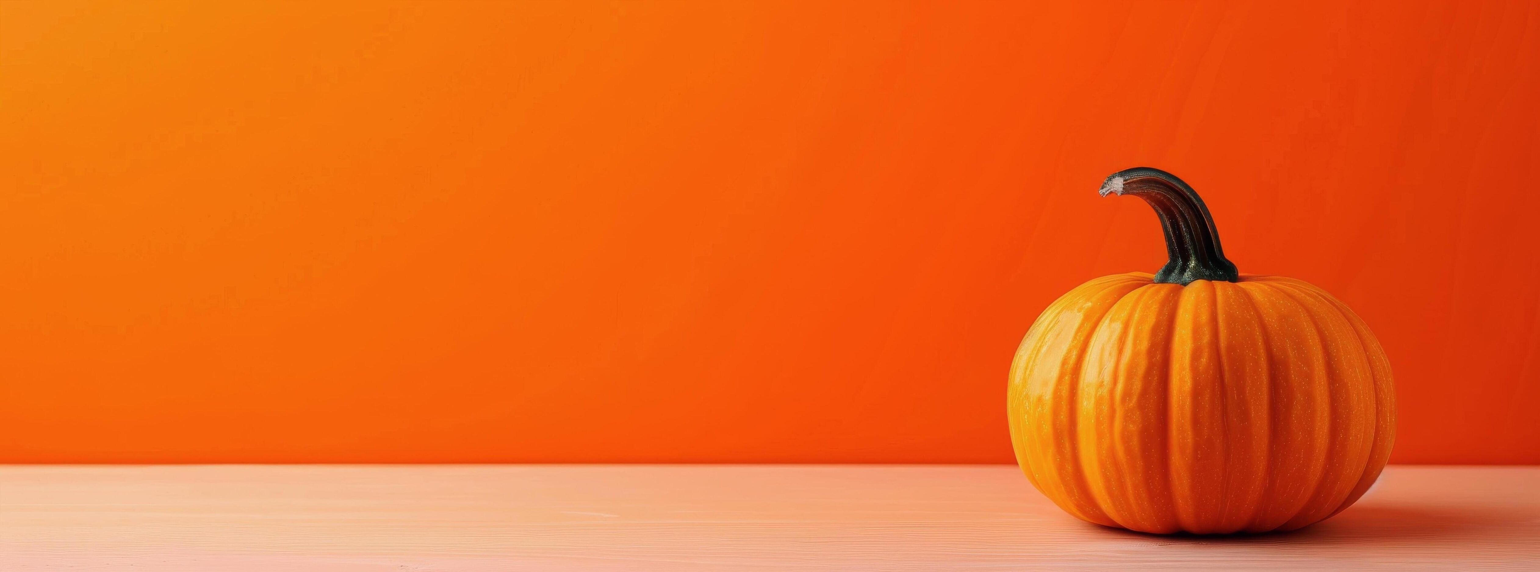 Vibrant Orange Pumpkin on White Surface Against Bright Orange Background in Autumn Stock Free