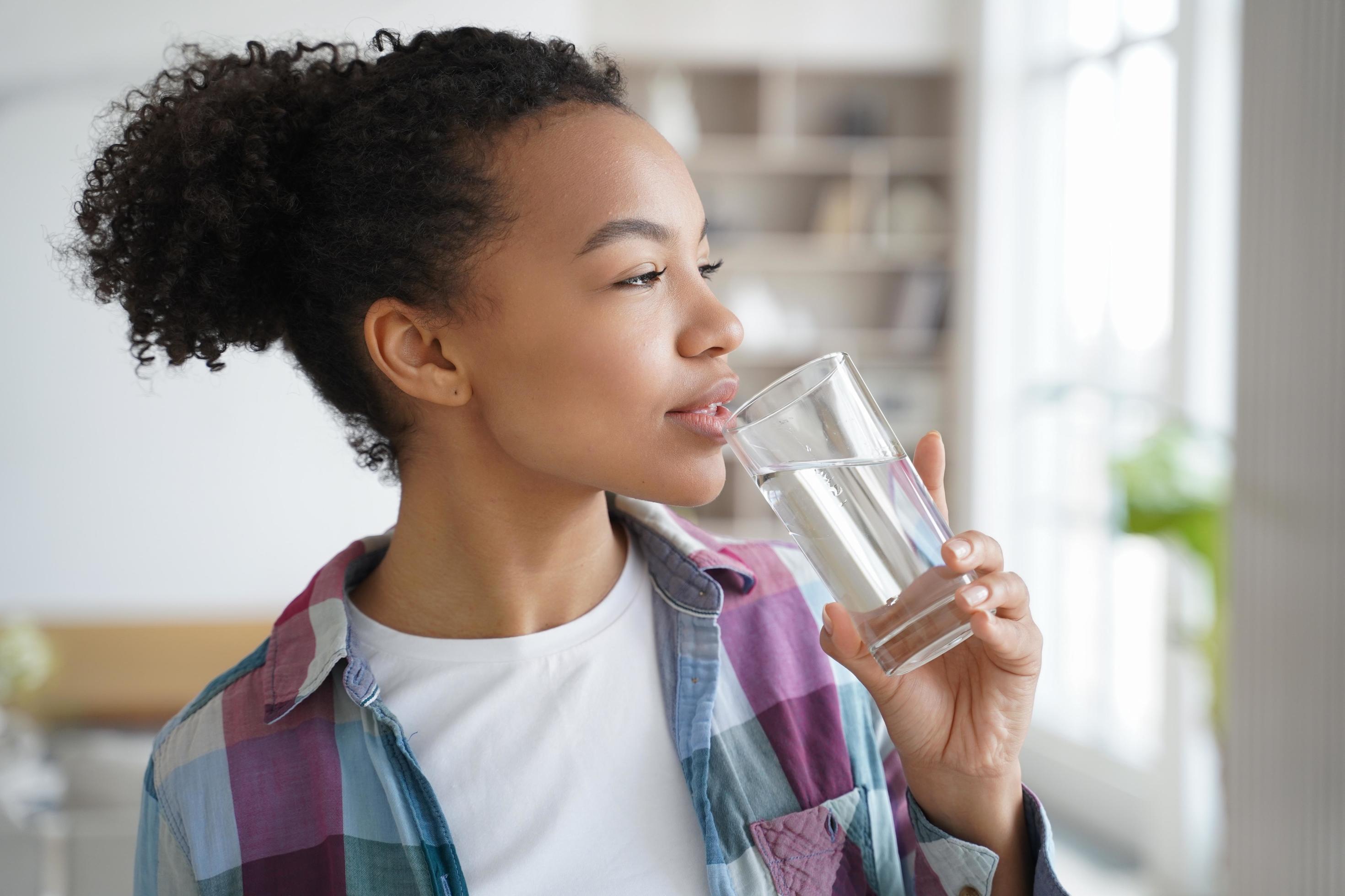 Mixed race young girl drink pure water from glass at home. Healthy lifestyle, morning routine Stock Free