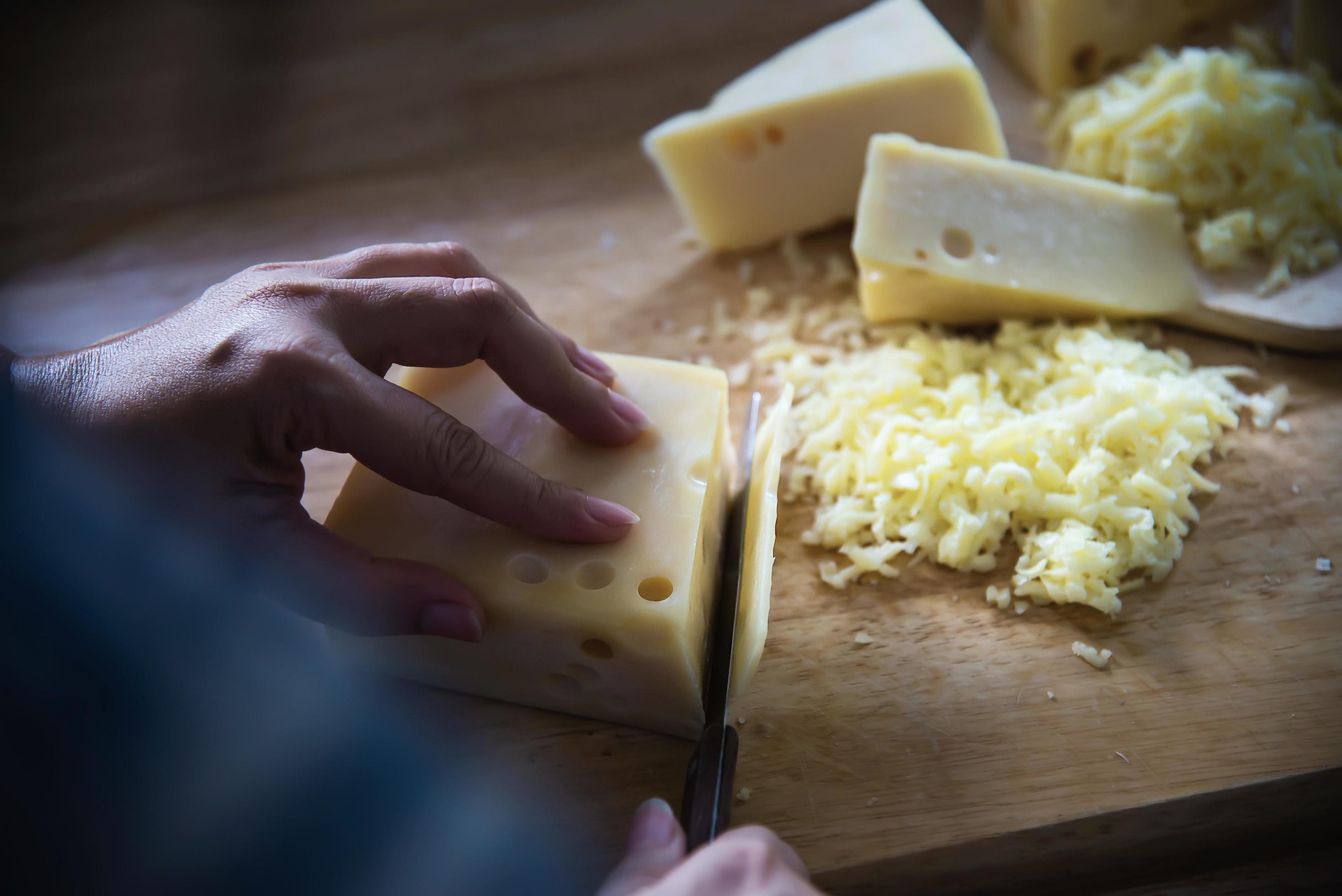 Woman preparing cheese for cook using cheese grater in the kitchen – people making food with cheese concept Stock Free