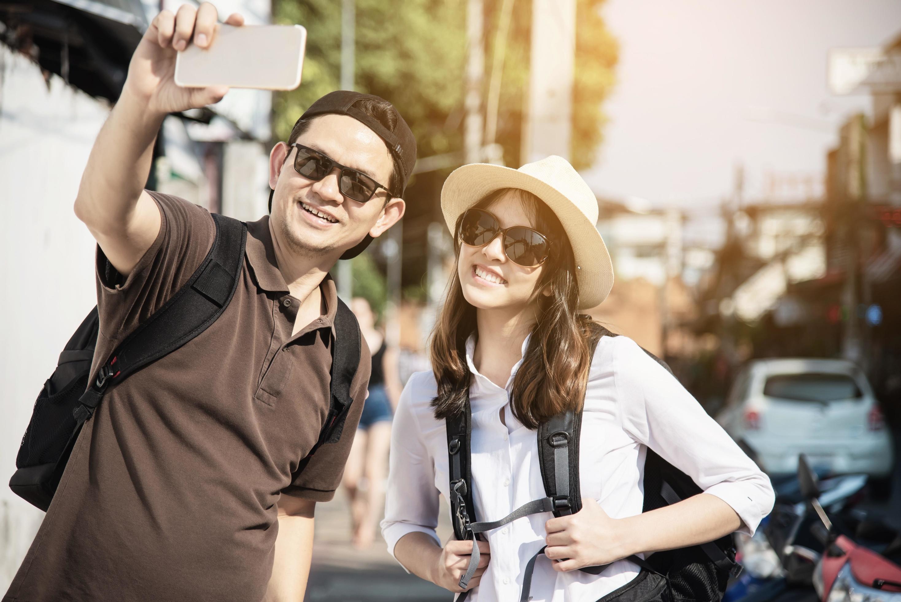 Asian backpack couple tourist holding city map crossing the road – travel people vacation lifestyle concept Stock Free