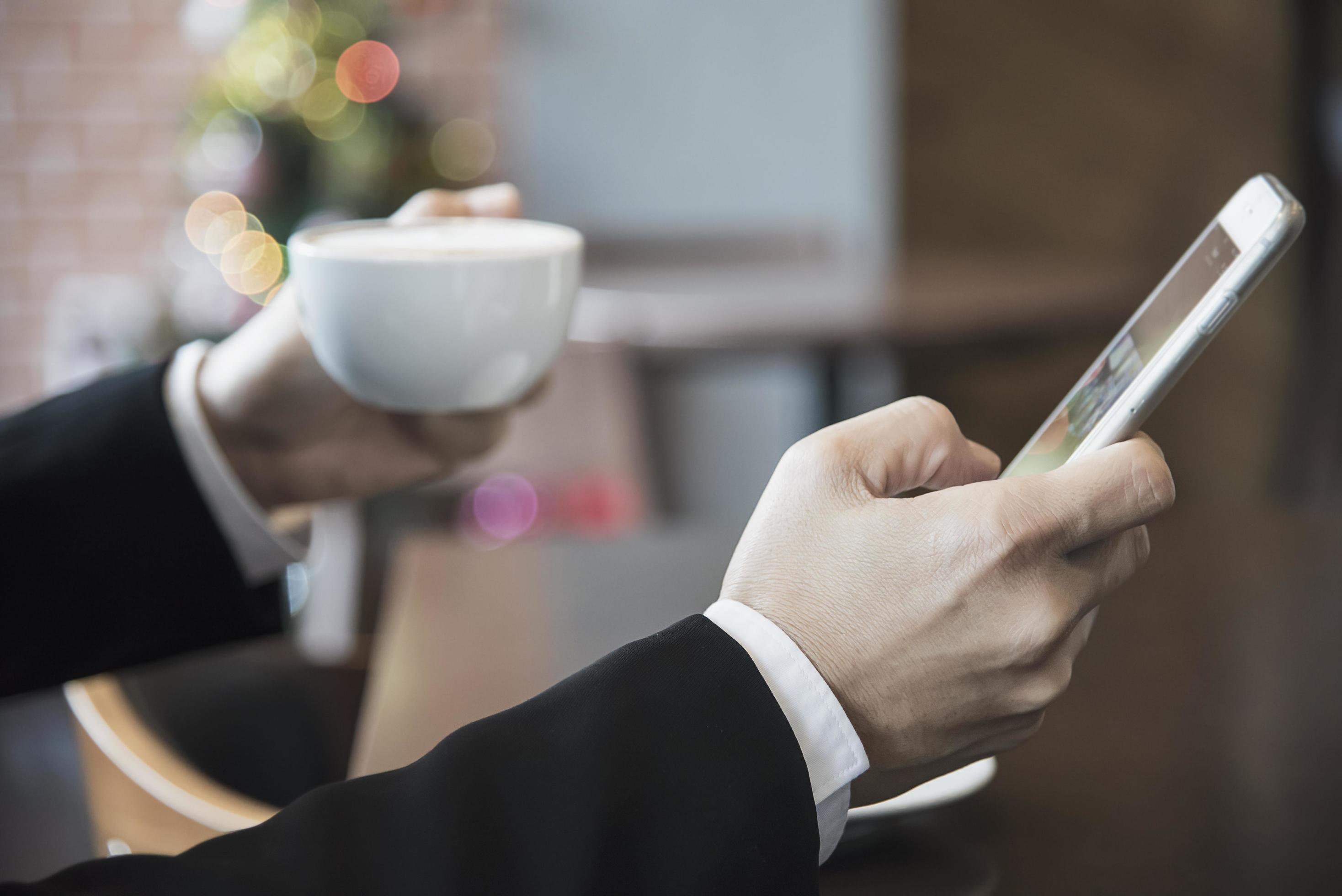 Business man using mobile phone while drinking coffee in coffee shop – modern life style business man in coffee shop concept Stock Free