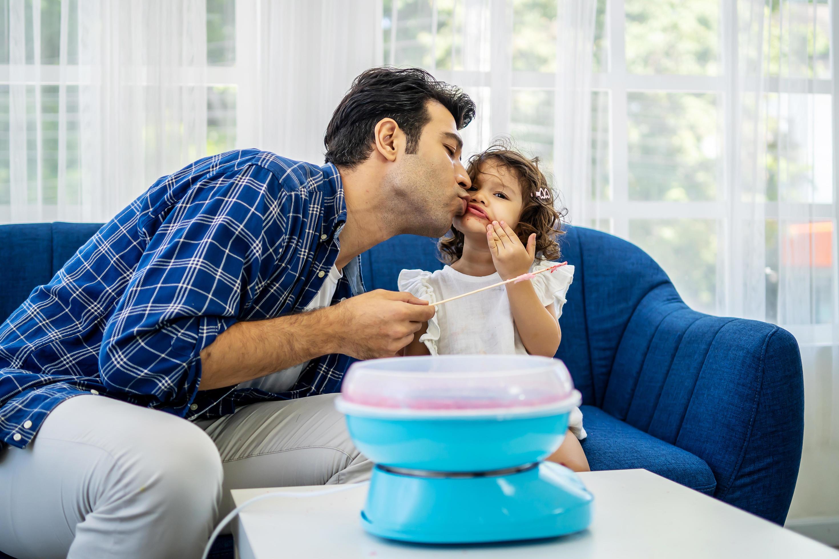 Caucasian family young father kissing his little daughter at mouth after eat cotton candy together on sofa at new house Stock Free