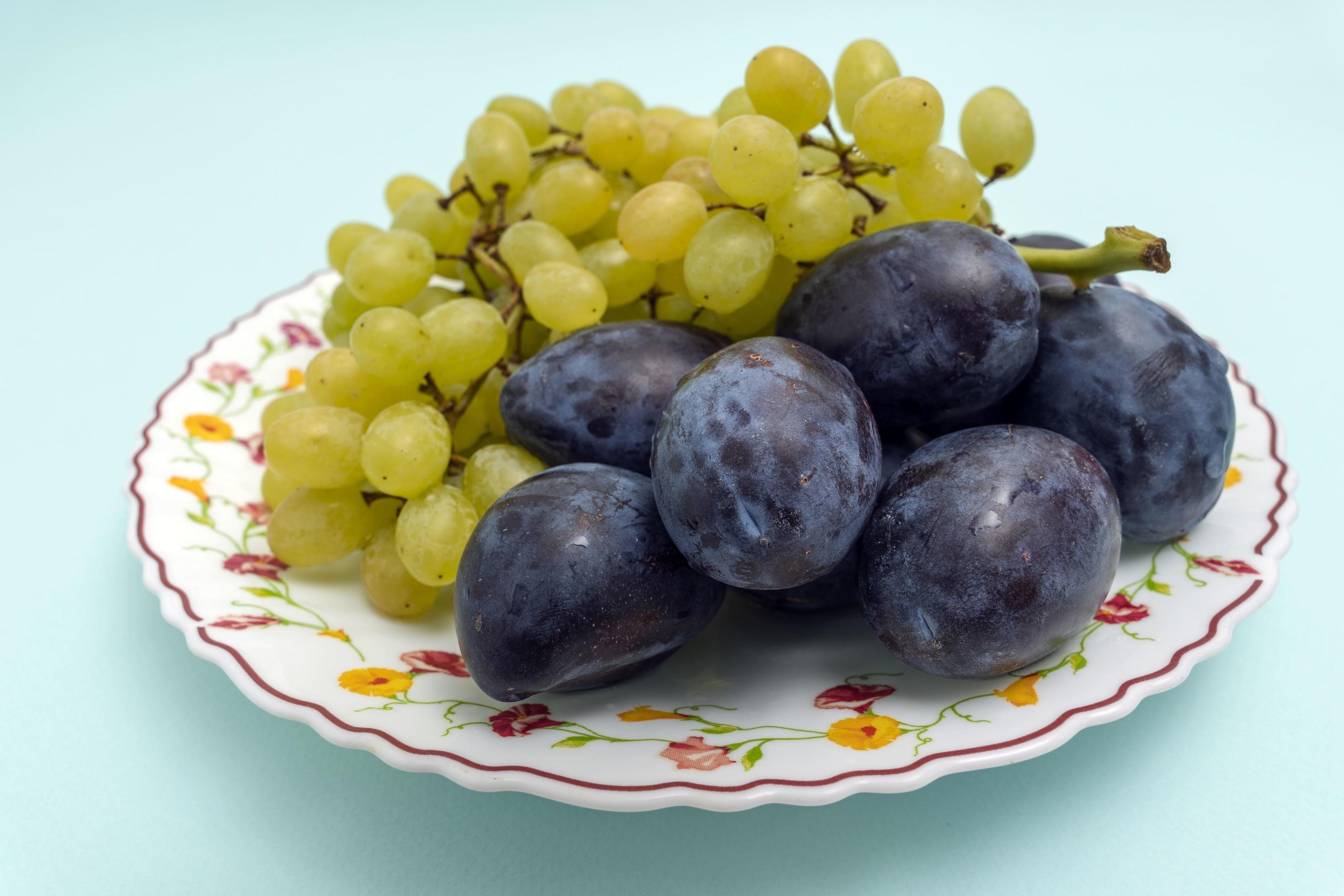 Ripe organic white grapes with round blue organic plums on a plate on a turquoise background, fruit, healthy food Stock Free