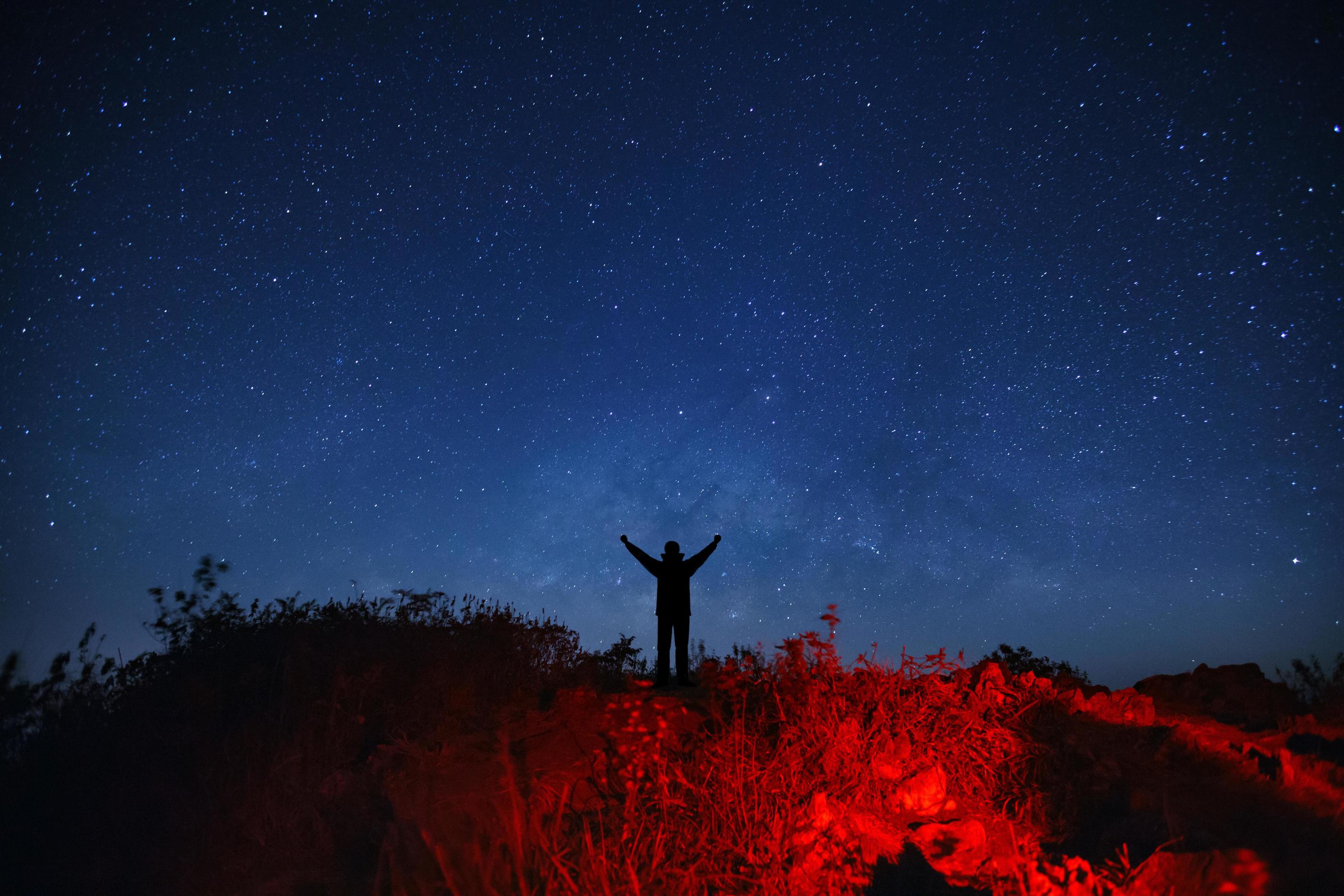 Landscape with milky way galaxy, Starry night sky with stars and silhouette of a standing sporty man with raised up arms on high mountain. Stock Free