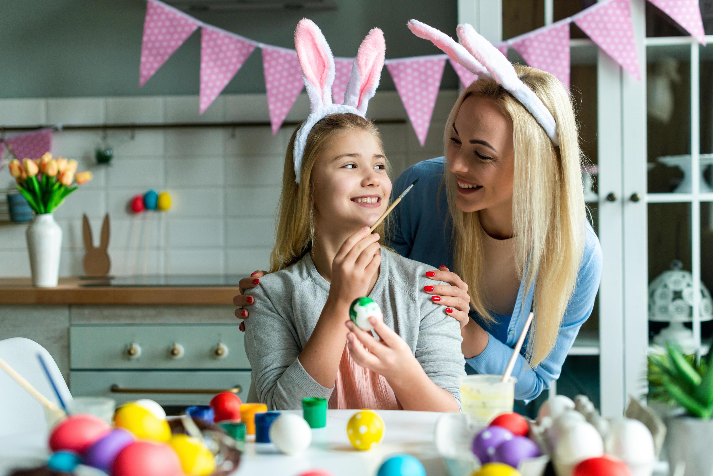 Happy holiday. A mother and her daughter are painting eggs. Family preparing for Easter. Cute little child girl is wearing bunny ears. Stock Free