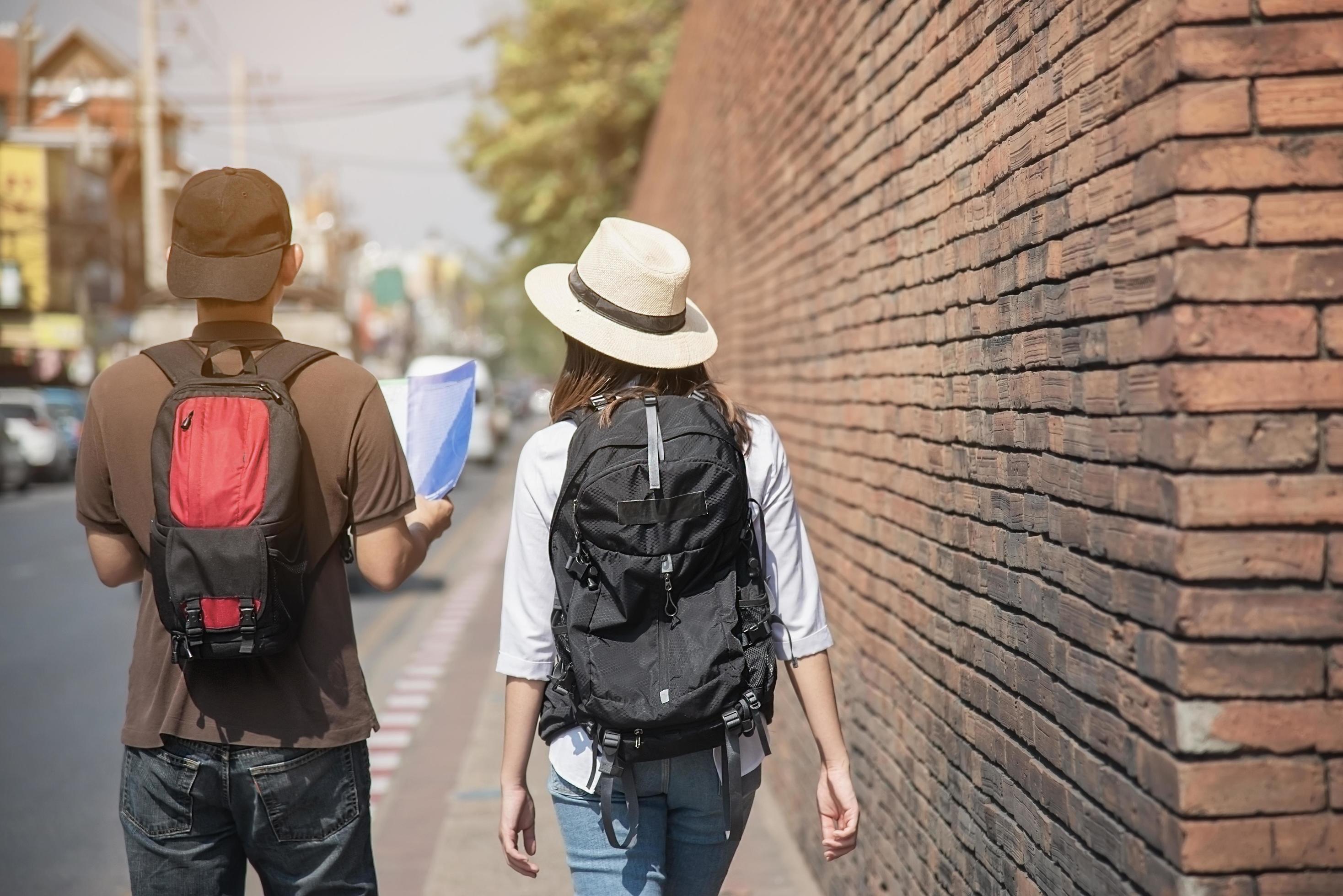 Asian backpack couple tourist holding city map crossing the road – travel people vacation lifestyle concept Stock Free