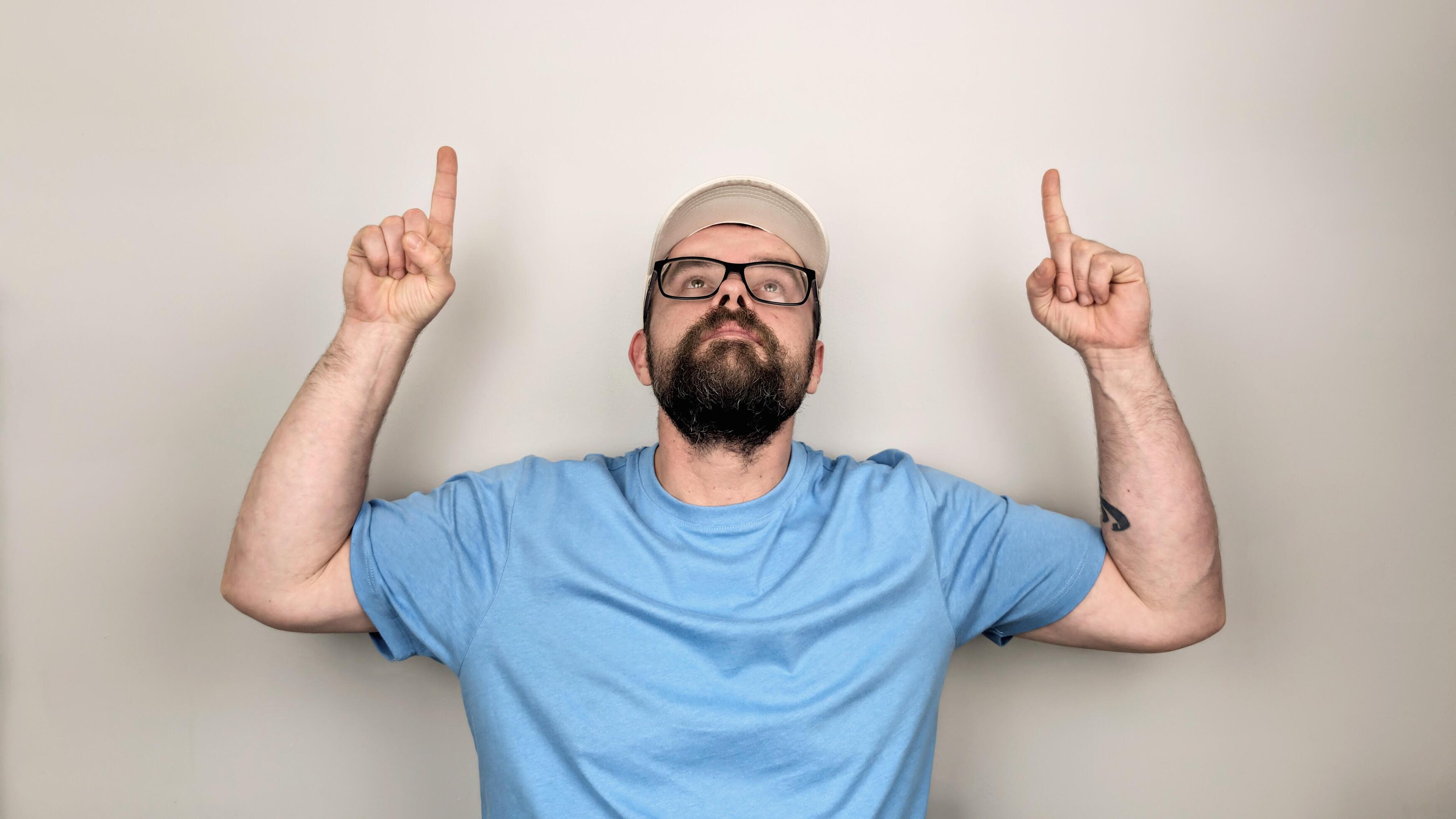 
									portrait of handsome bearded man with straw hat and glasses smiling, pointing up gesture, wearing blue shirt , isolated on white background Stock Free