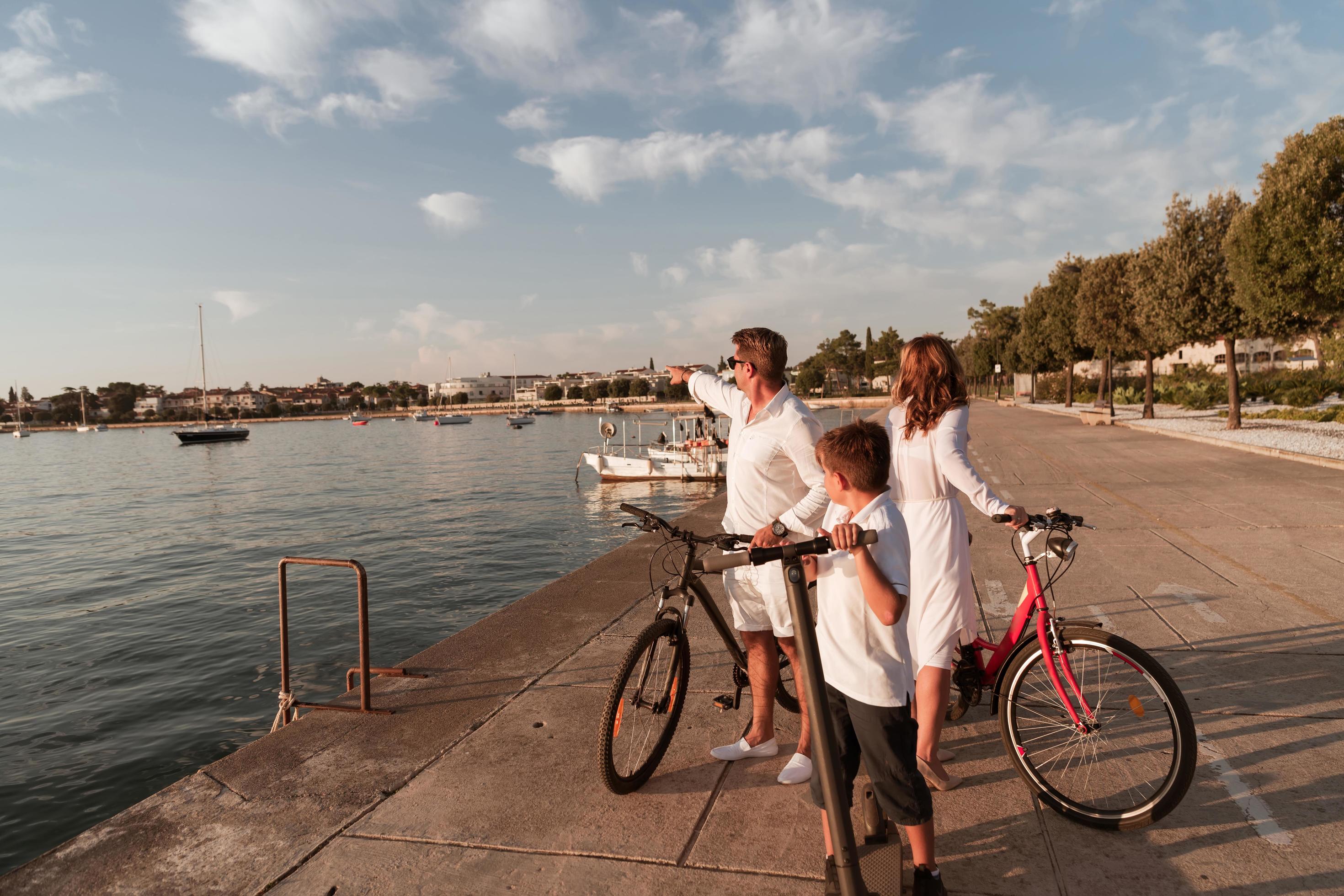 Happy family enjoying a beautiful morning by the sea together, parents riding a bike and their son riding an electric scooter. Selective focus Stock Free