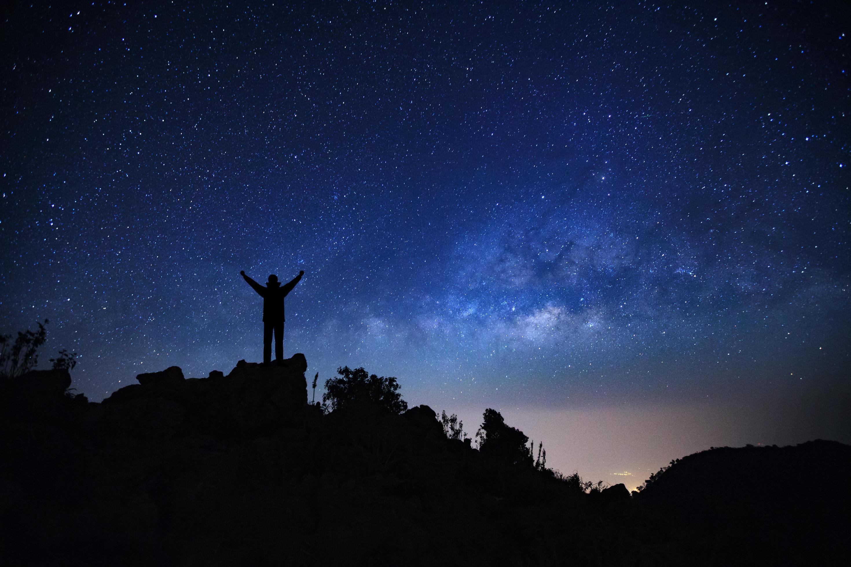 Landscape with milky way galaxy, Starry night sky with stars and silhouette of a standing sporty man with raised up arms on high mountain. Stock Free