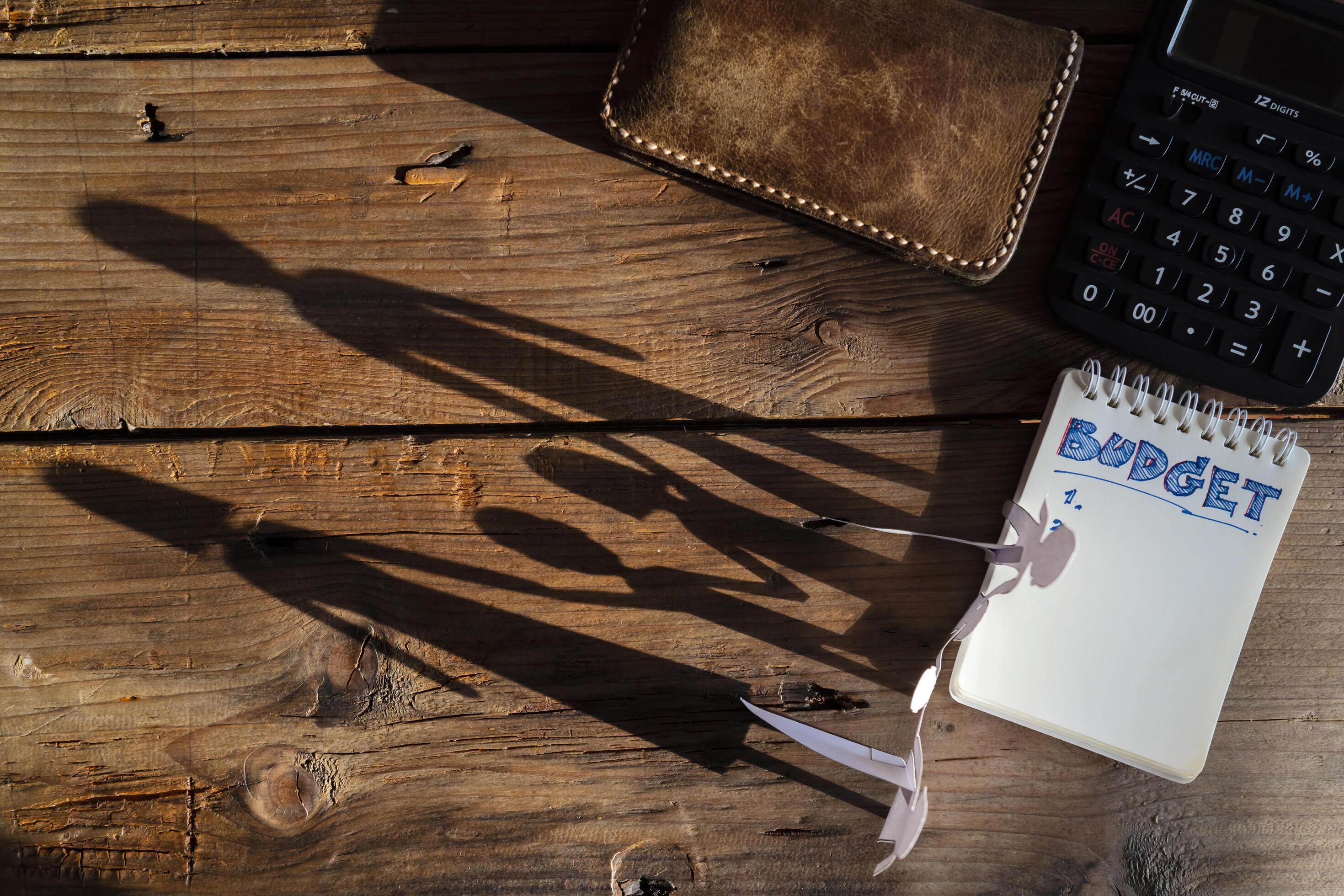 Budget planing concept. Top view of notepad with word budget, calculator, cup of coffee, family silhouette, pouch on wooden background Stock Free