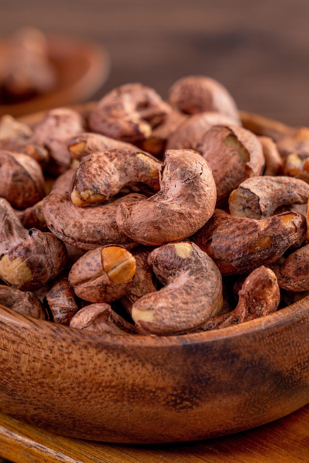 Cashew nuts with peel in a wooden bowl on wooden tray and table background, healthy raw food plate. Stock Free