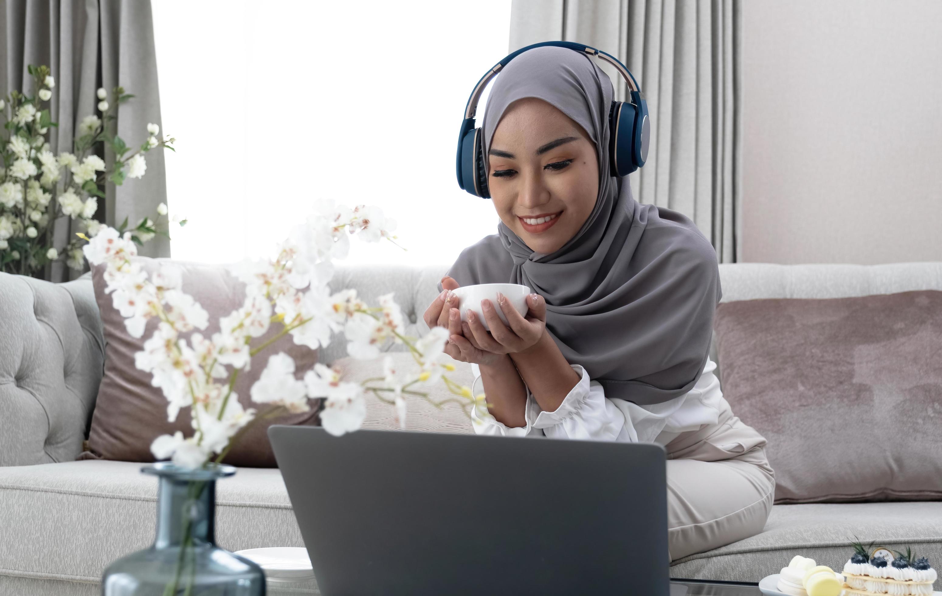 Domestic Lifestyle. Happy Muslim Woman Using Laptop At Home, Watching Movie And Drinking Coffee, Relaxing On Couch In Living Room, Side View Stock Free